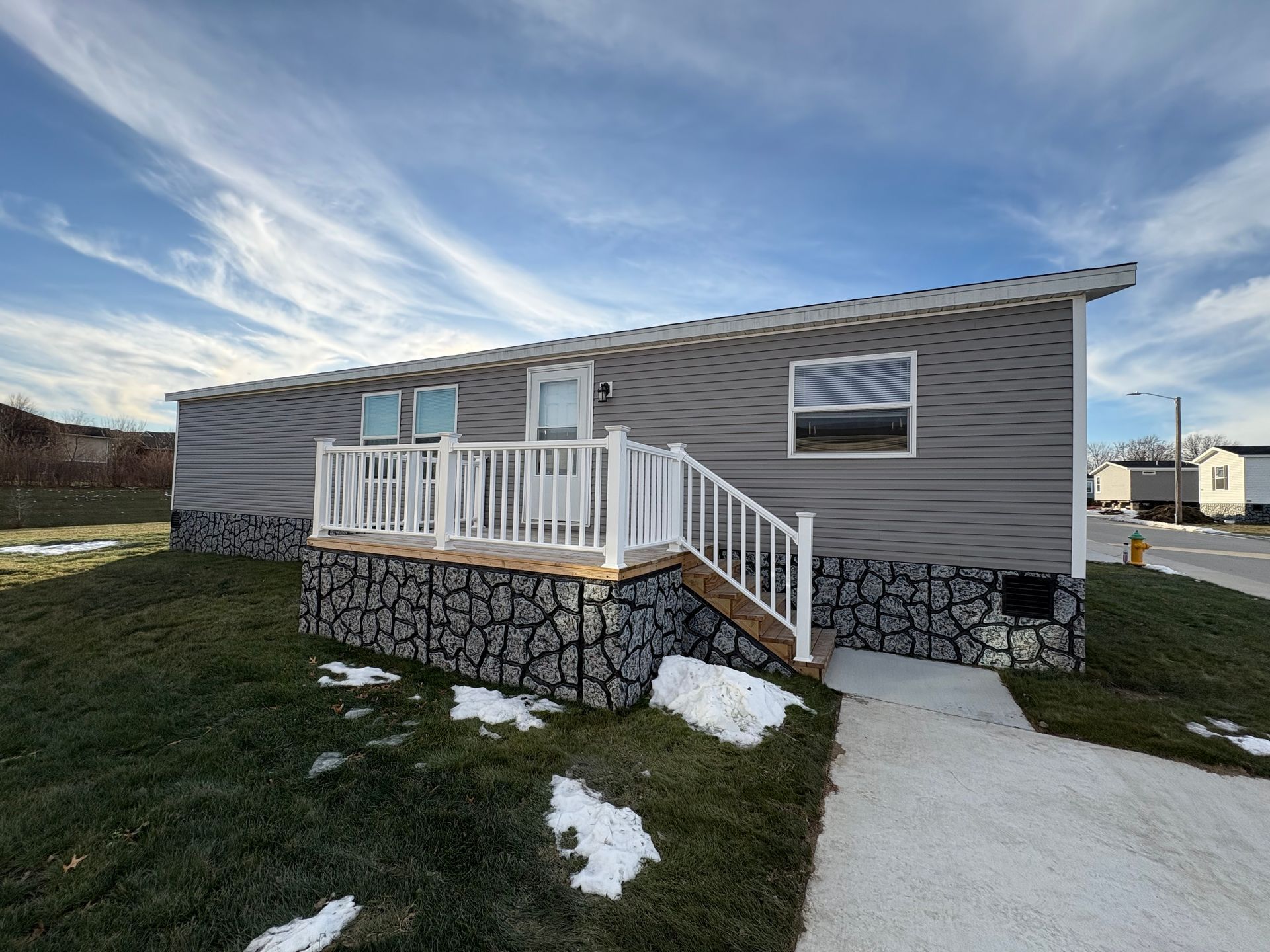 Gray house with a small porch, stone base, and blue sky.