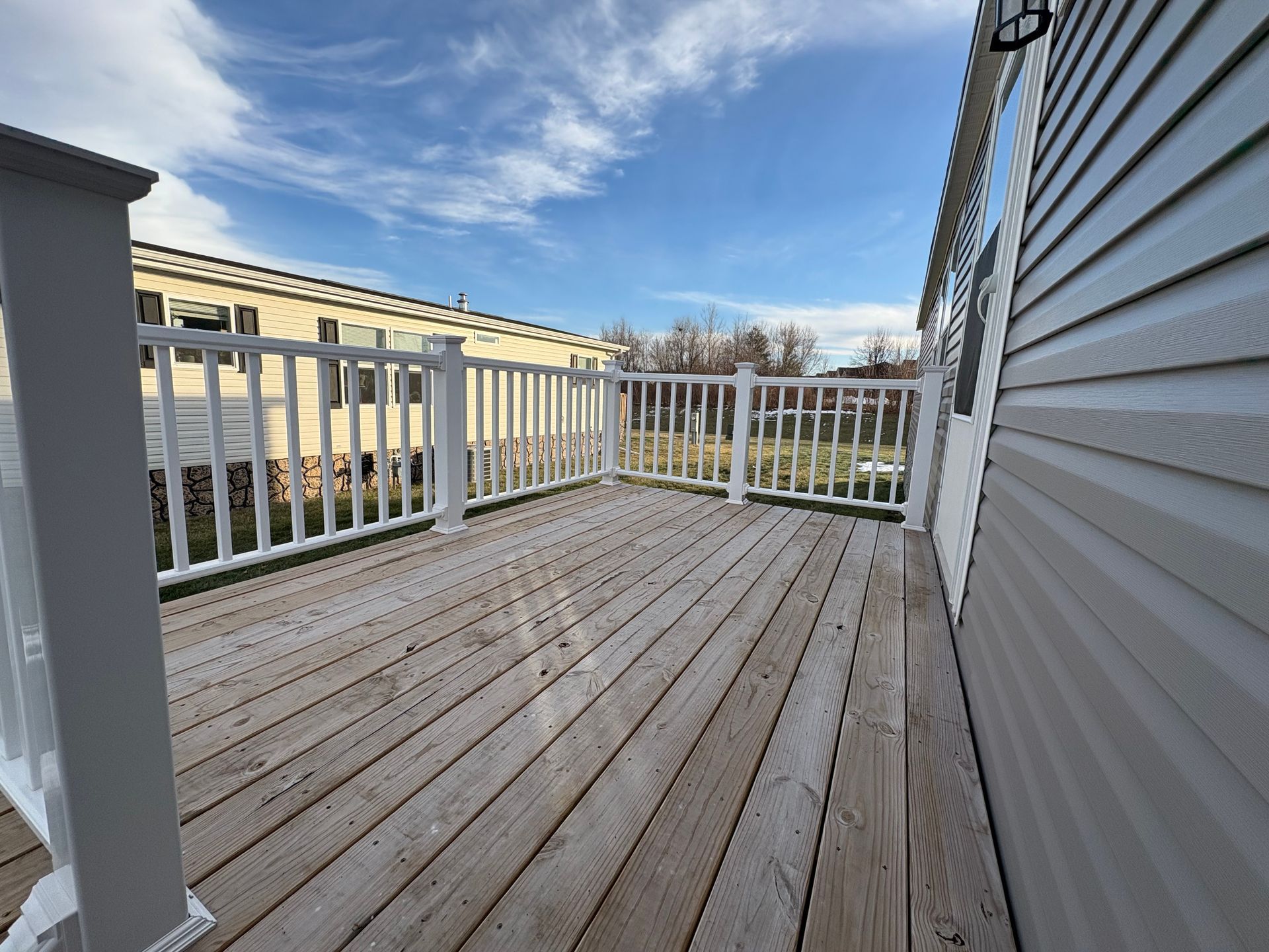 Wooden deck with white railing next to a building, blue sky in background.