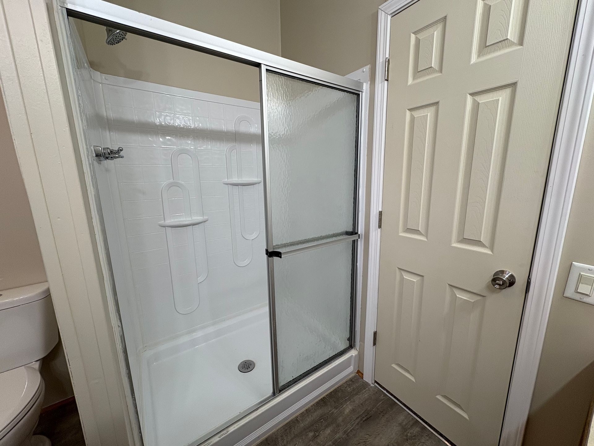 A white shower stall with sliding glass doors, next to a closed door, and a toilet partially visible.