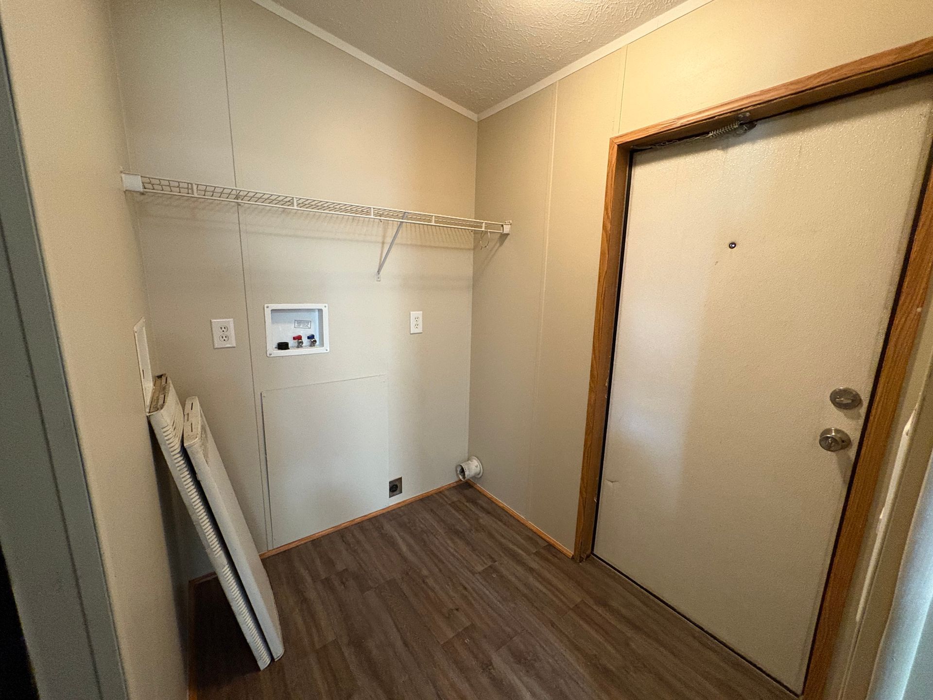 Laundry room with light walls, wooden floor, open shelf, white door, and washer/dryer hookups.