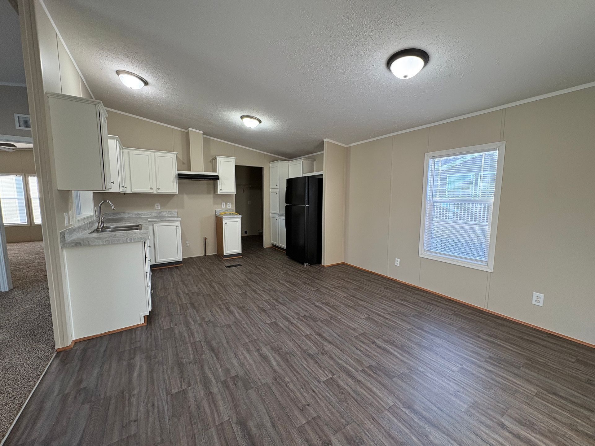 Interior view of a kitchen with white cabinets, dark refrigerator, and wood-look flooring. Window with natural light.