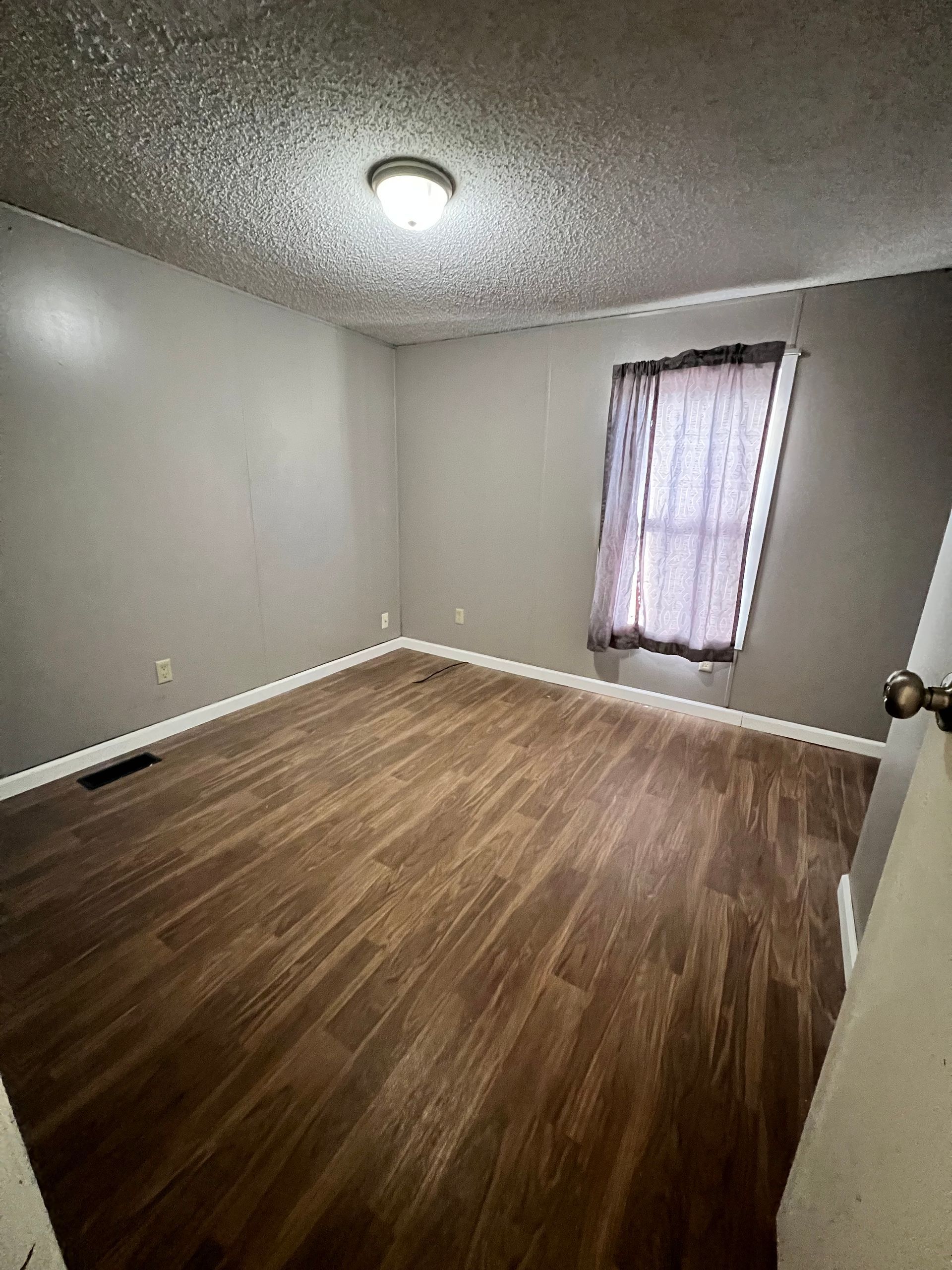 Empty room with wood-look flooring, gray walls, and a window with a curtain.