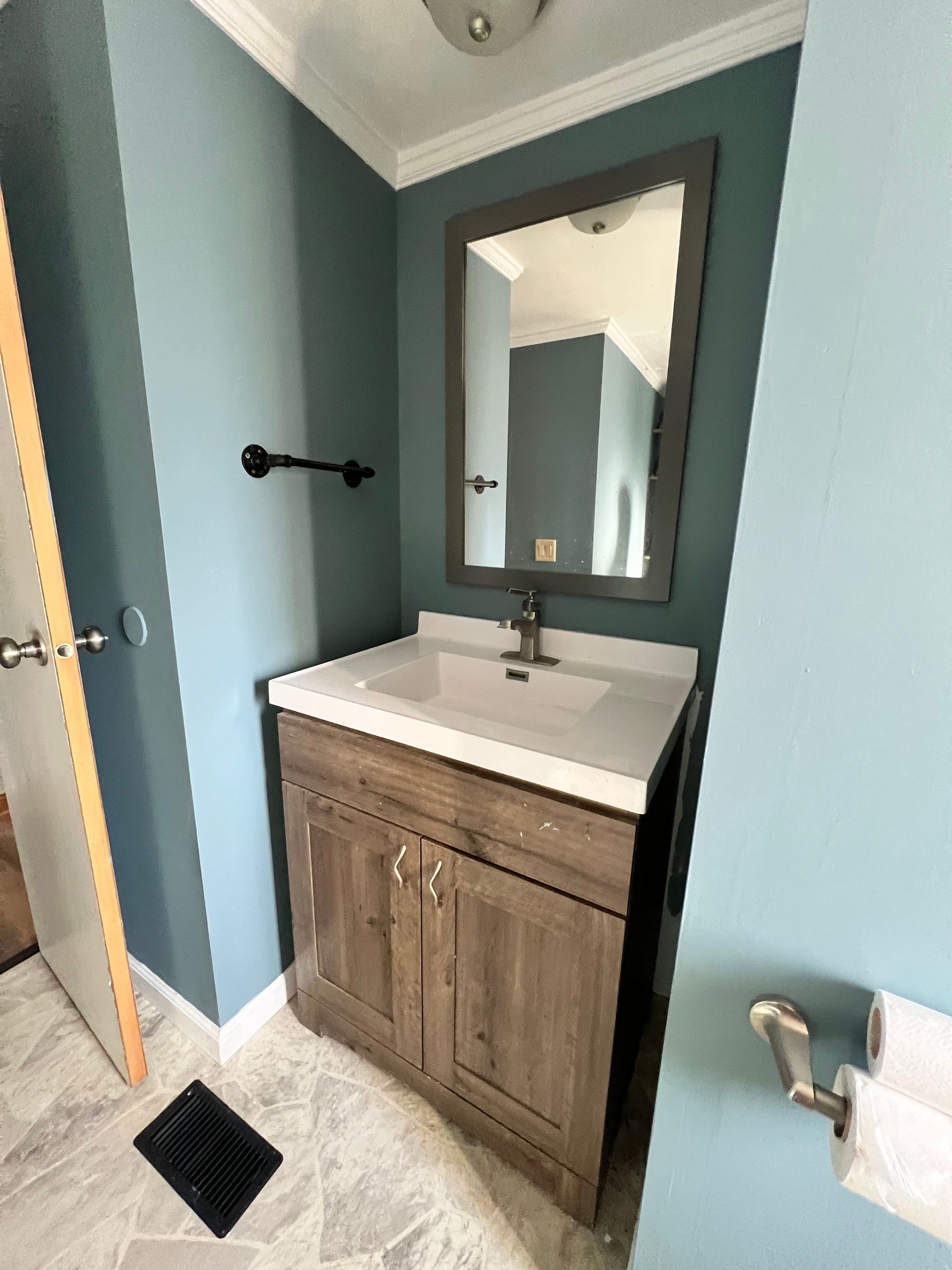 Bathroom with blue walls, wood vanity, white sink, and dark-framed mirror.