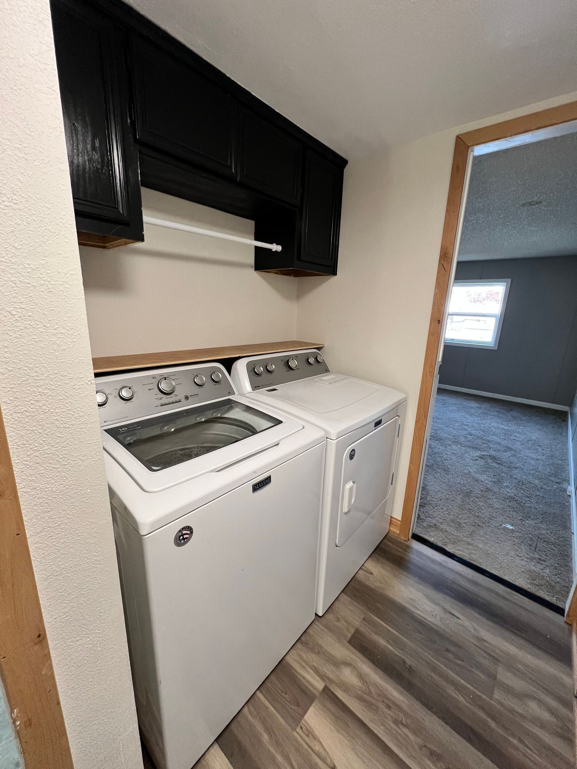 Laundry room with a washing machine and dryer, black cabinets, and a doorway to another room.