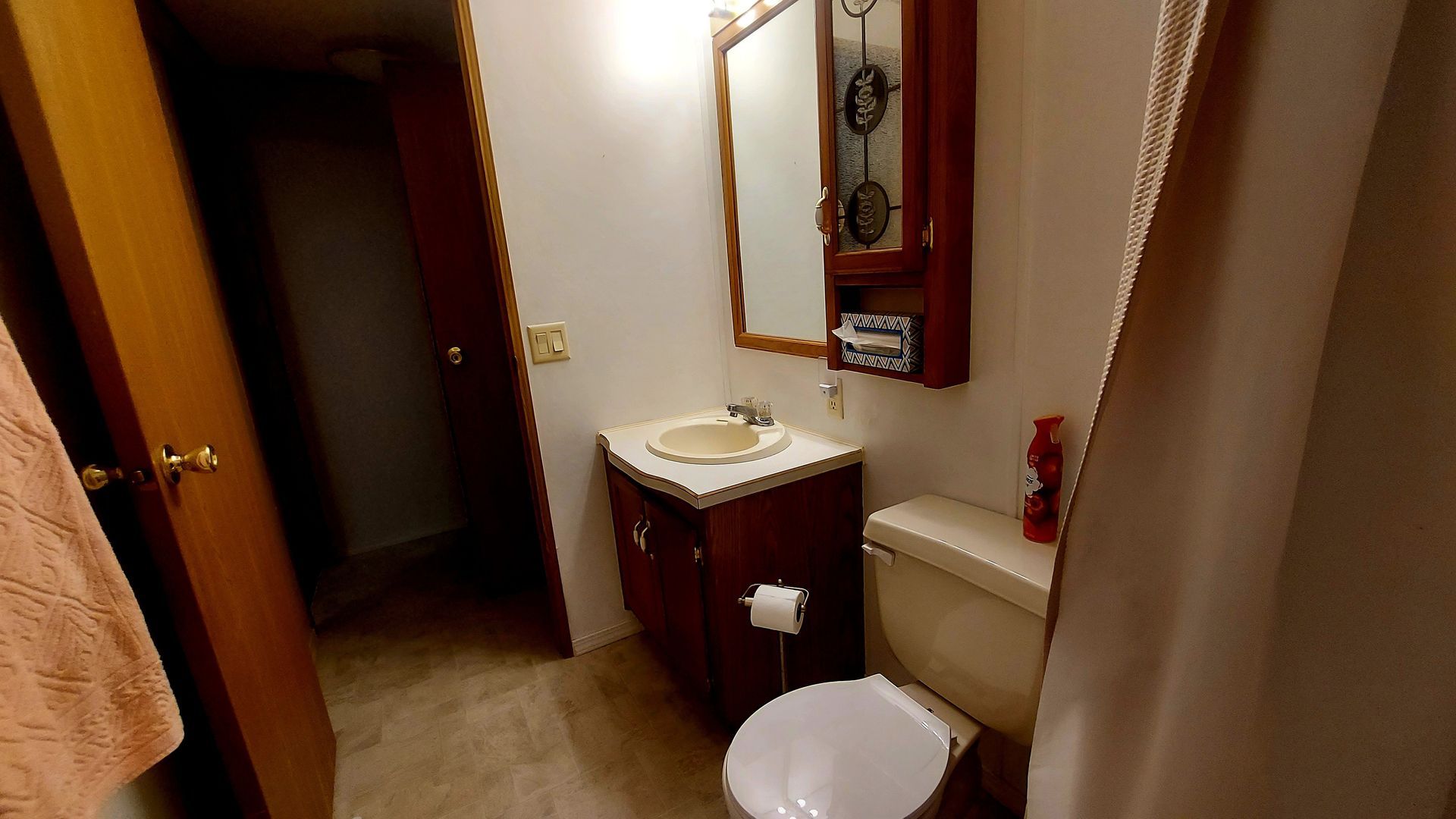 Bathroom with toilet, sink, mirror, cabinet, and open doorway to another room.