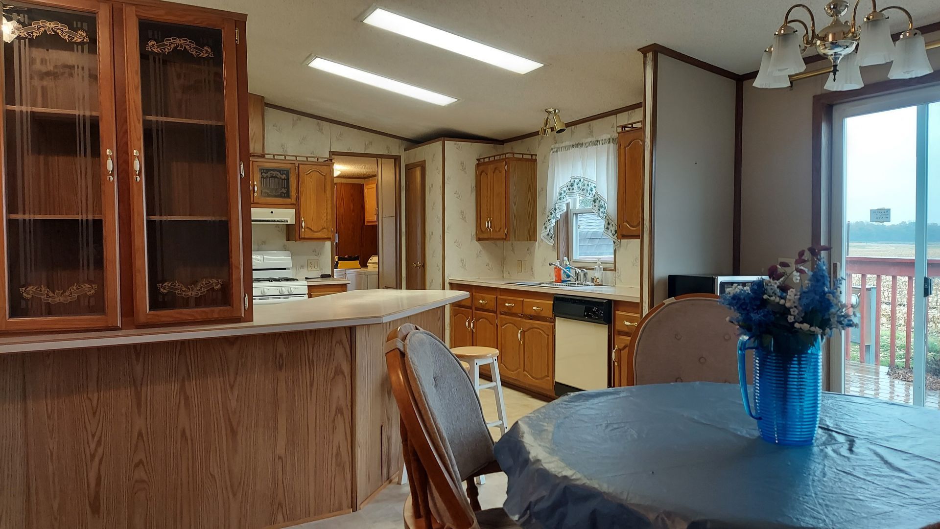 Interior view of a kitchen and dining area with wooden cabinets, a table, and a sliding glass door.
