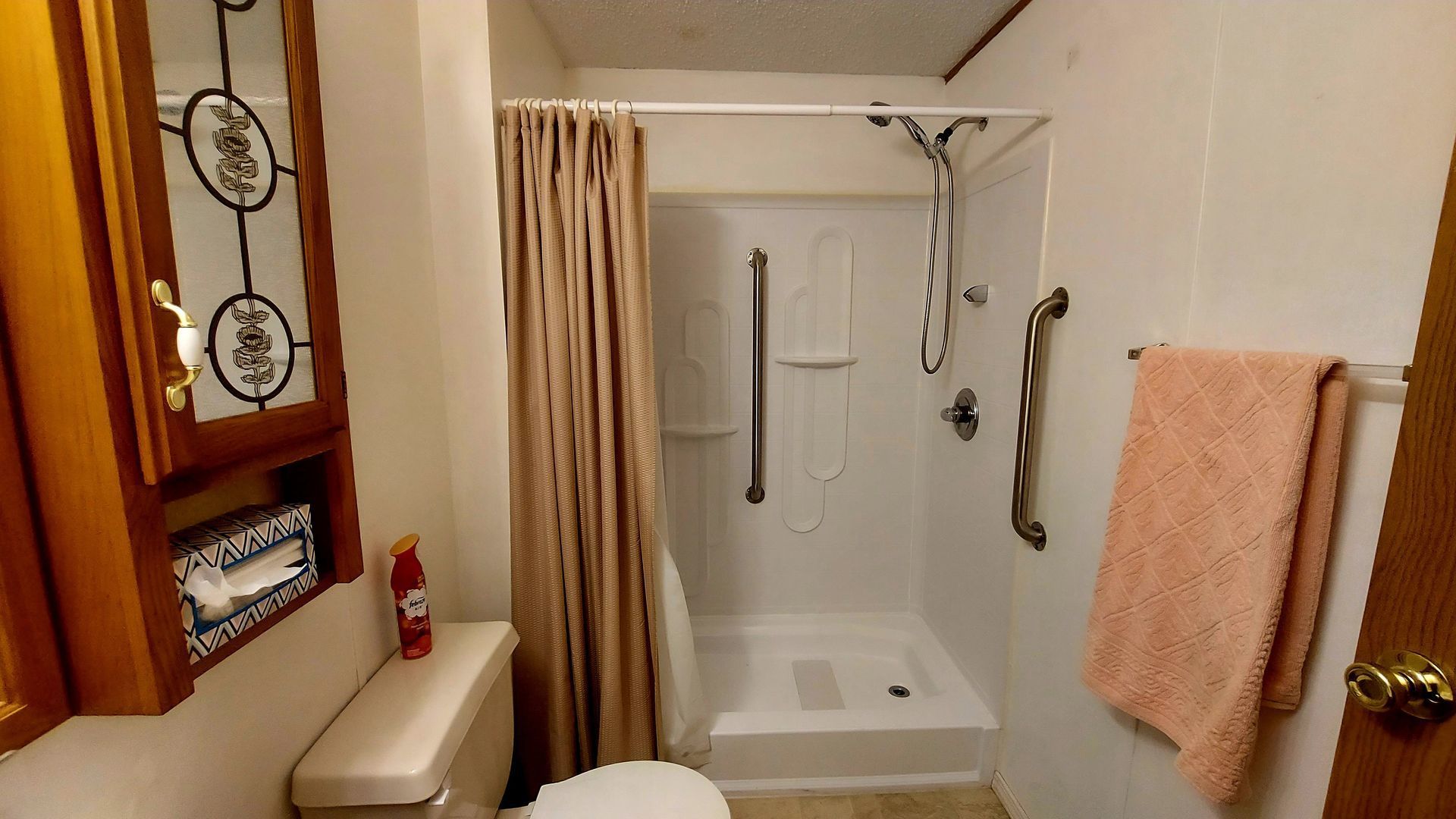 Small bathroom with white shower, tan curtain, toilet, cabinet, and towel.