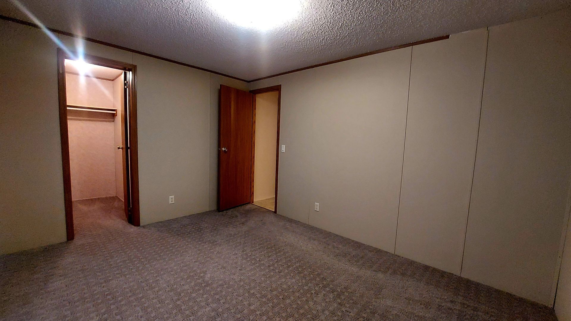 Empty bedroom with gray carpet, beige walls, and two open doorways.