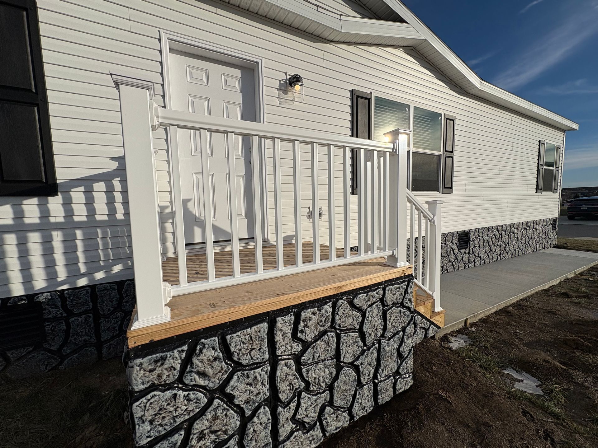 White house with a small porch, featuring a white railing and stone-look foundation.