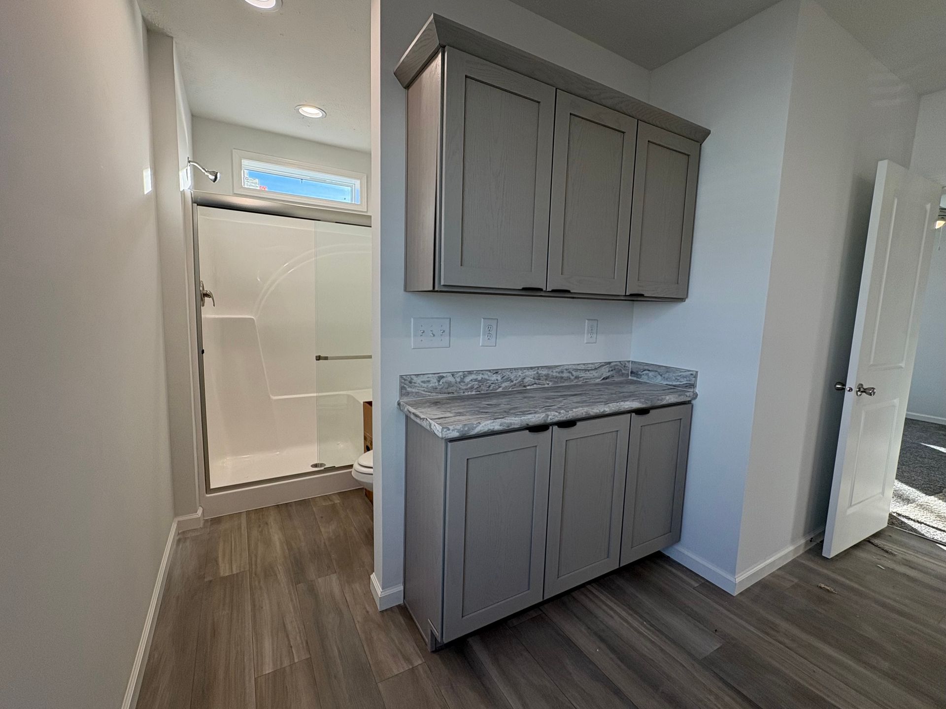 Bathroom with gray cabinets, a marble countertop, and a shower with a small window.