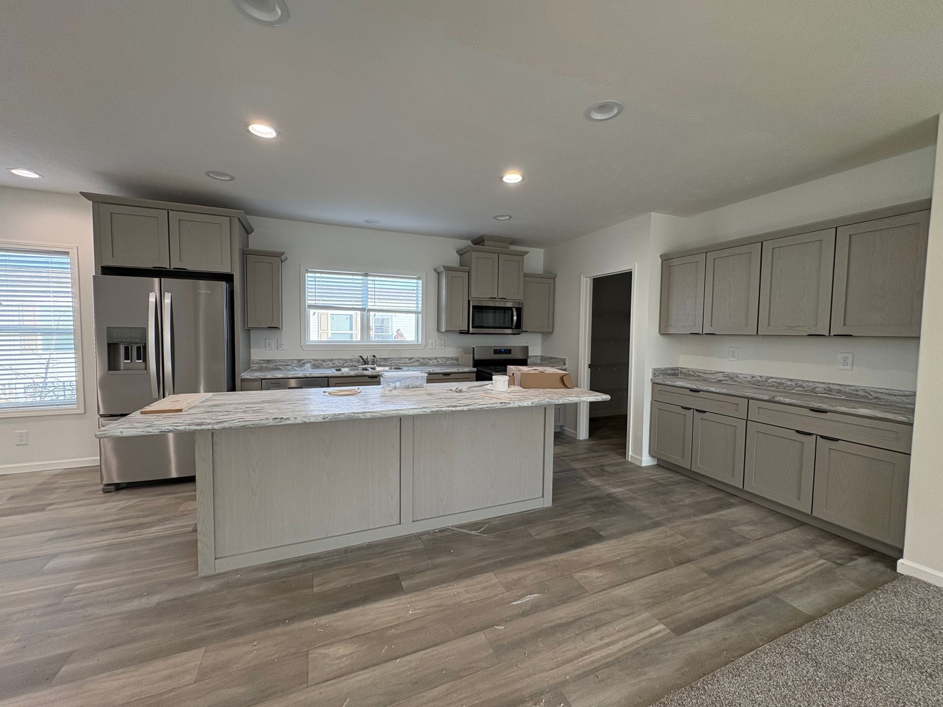Spacious kitchen with gray cabinets, island, stainless steel appliances, and wood-look flooring.