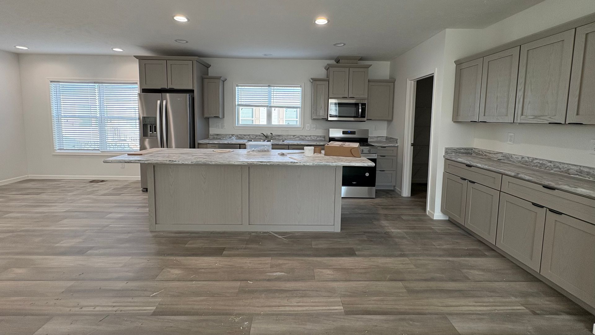 Newly constructed kitchen with grey cabinets, island, and stainless steel appliances.