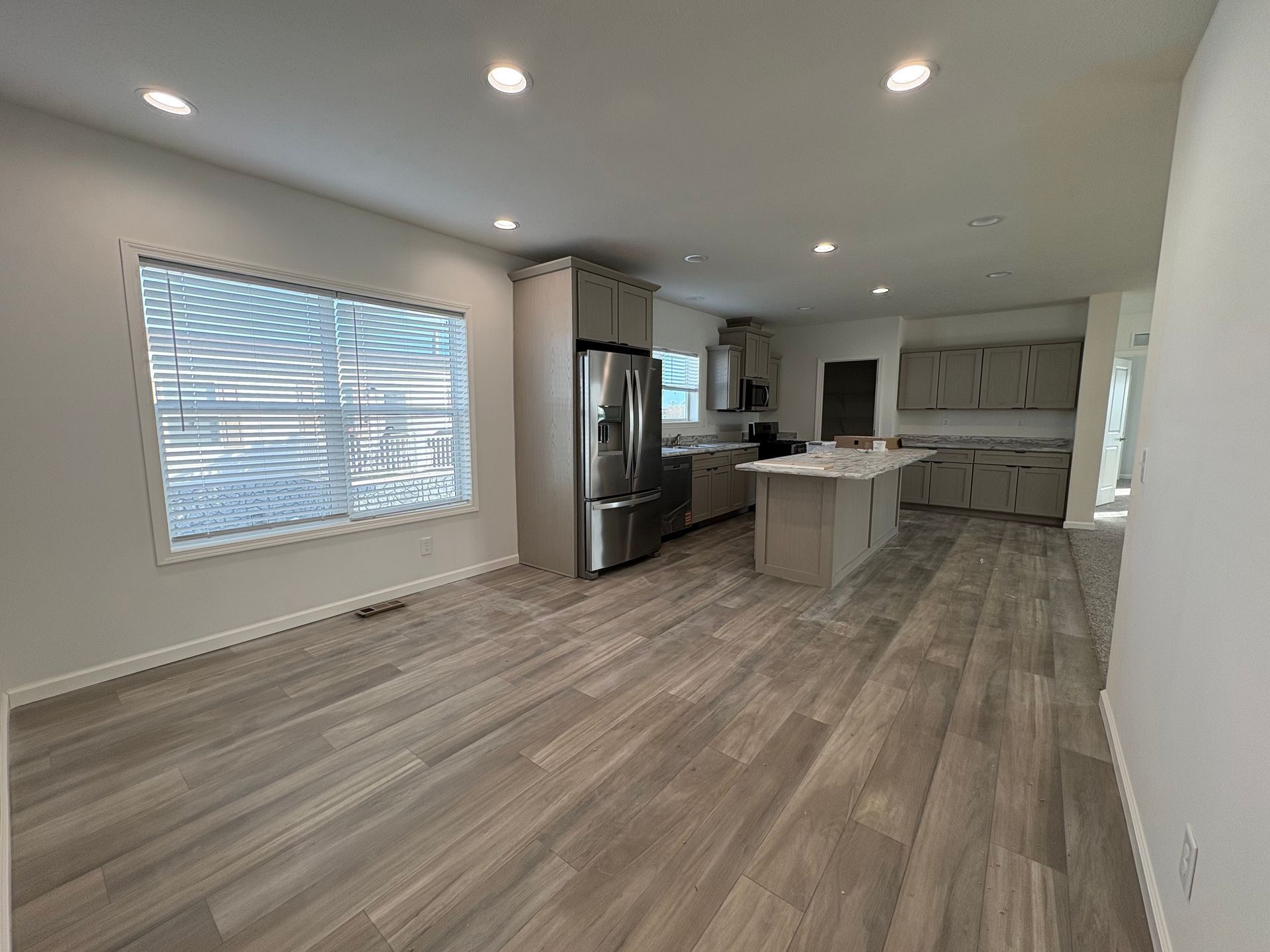 Open-plan kitchen with gray cabinets, island, stainless steel appliances, and wood-look tile flooring.