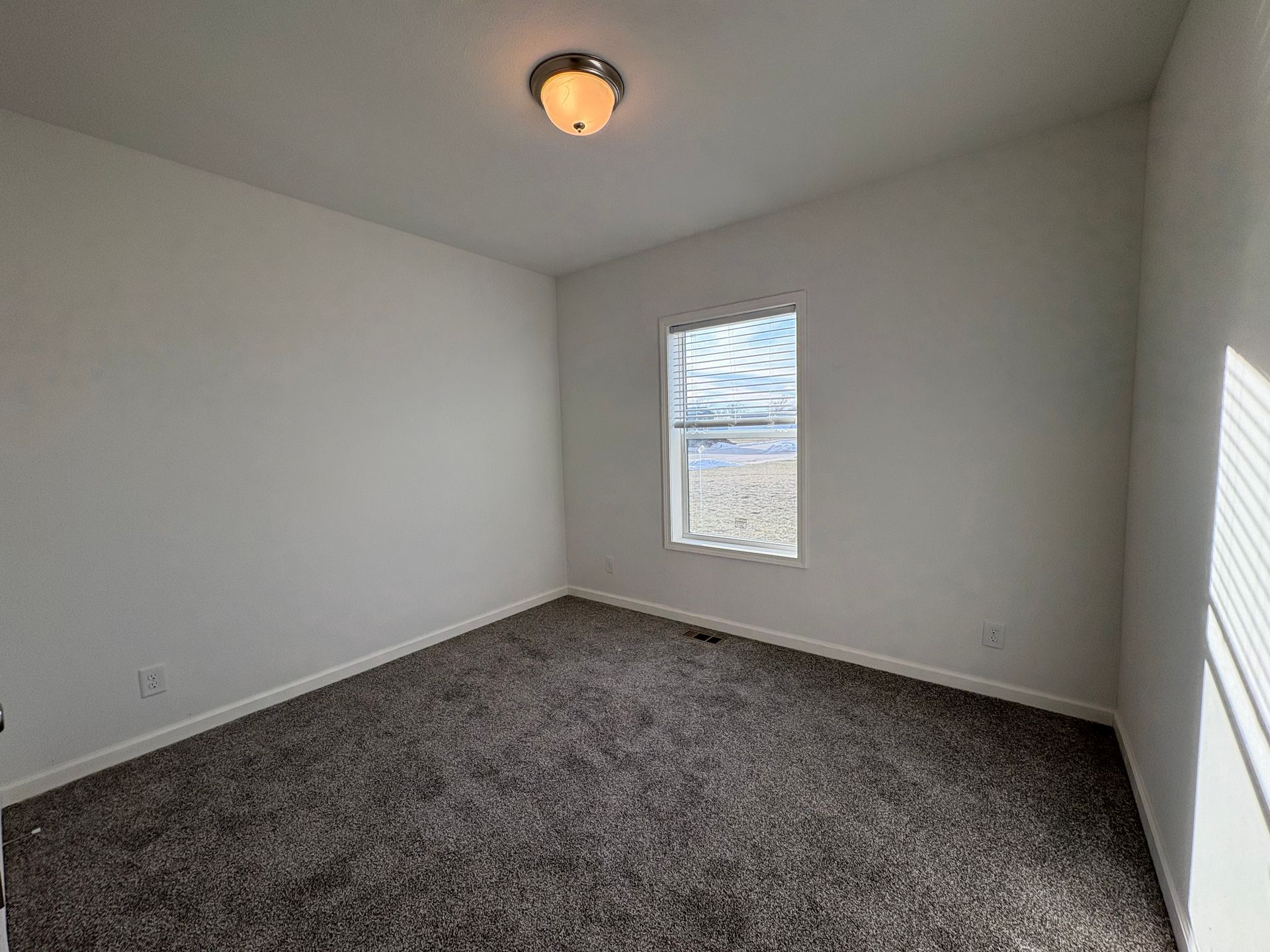 Empty room with gray carpet, a small window, and a ceiling light.