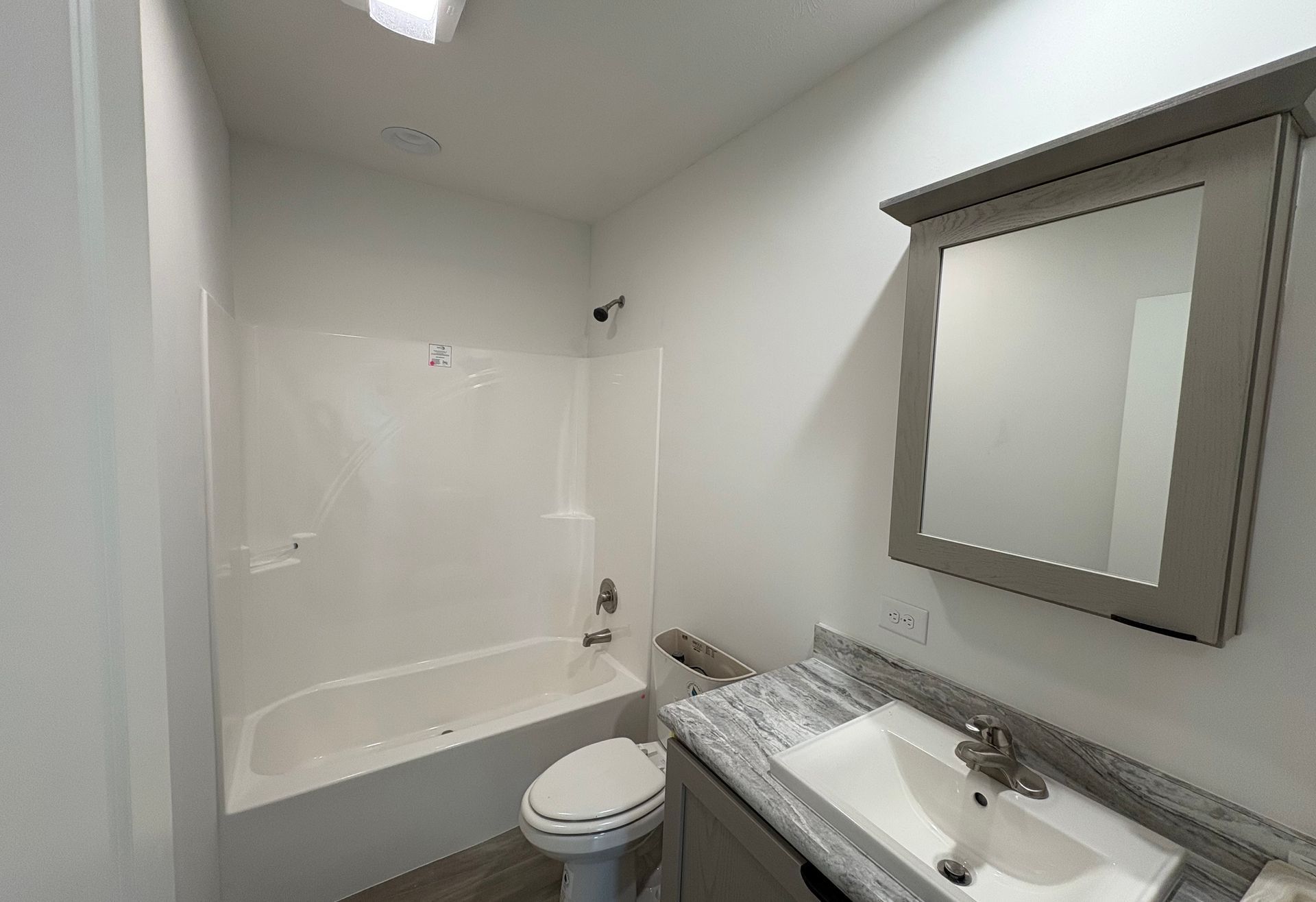 Bathroom with white walls, a bathtub, toilet, vanity, and a mirror.
