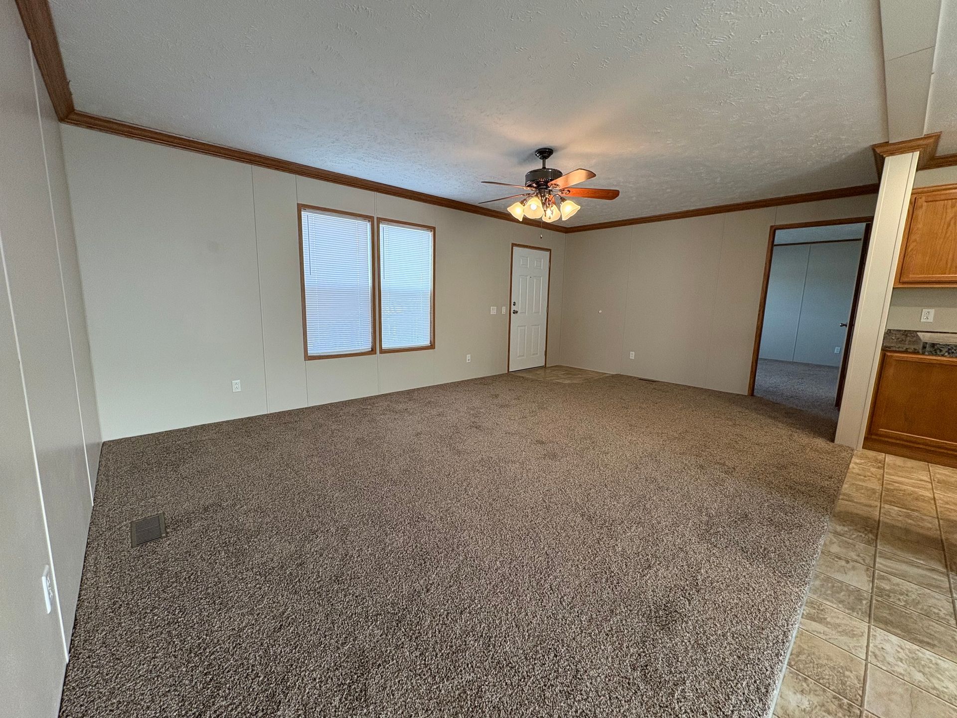 Empty living room with brown carpet, tan walls, and a ceiling fan.