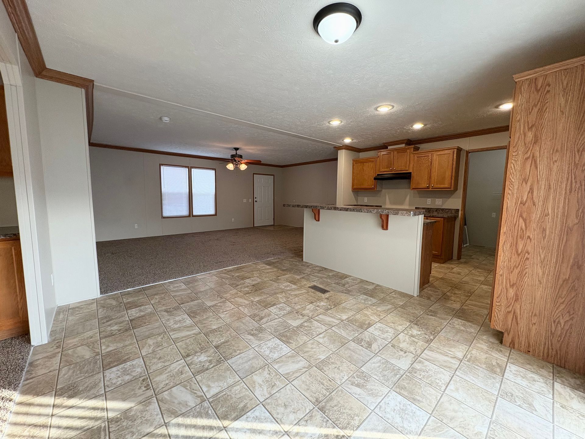 Open-concept living space with kitchen, brown cabinets, and beige tile floor.