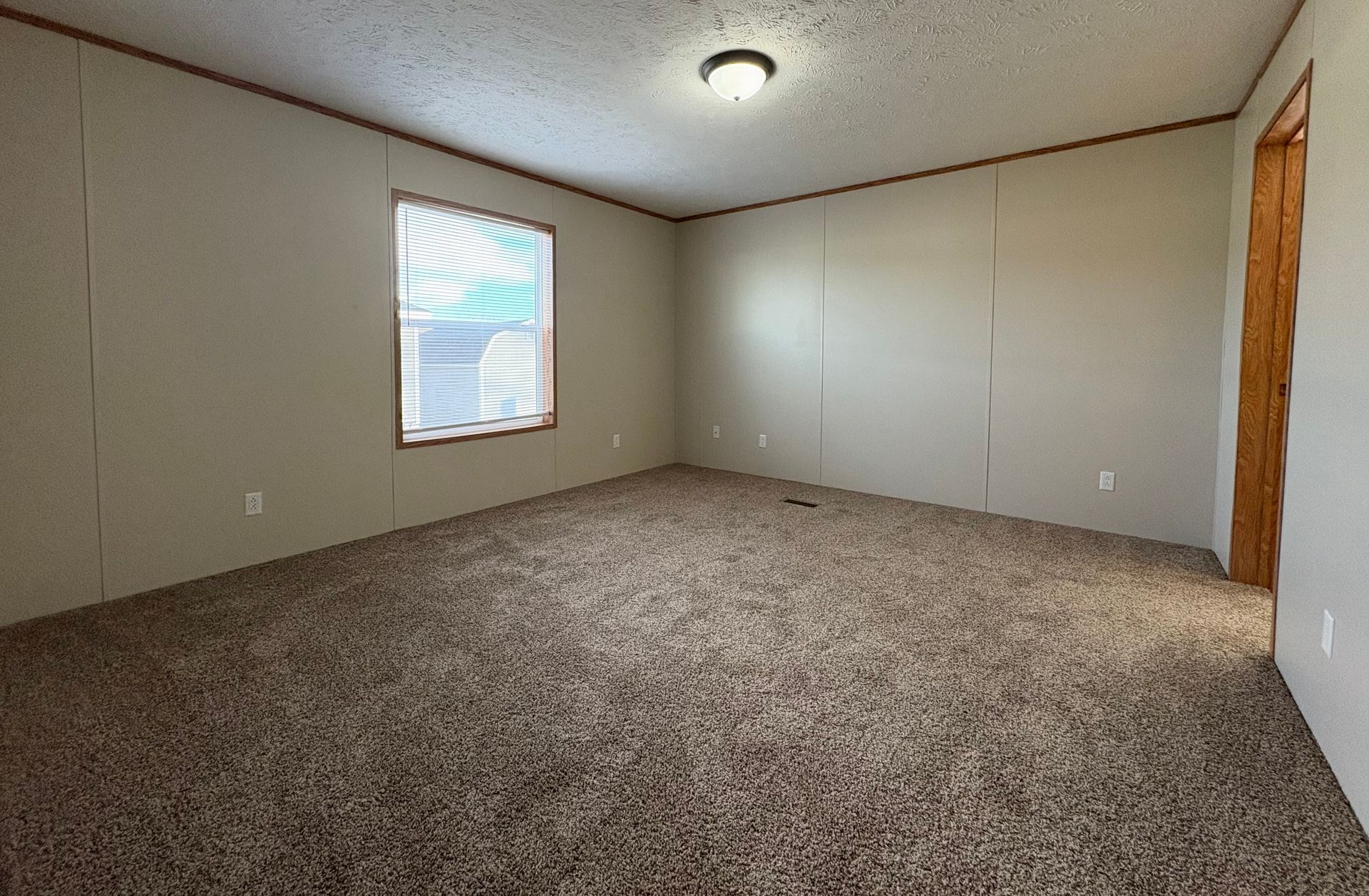 Empty room with brown carpet, light-colored walls, window with blinds, and a door.