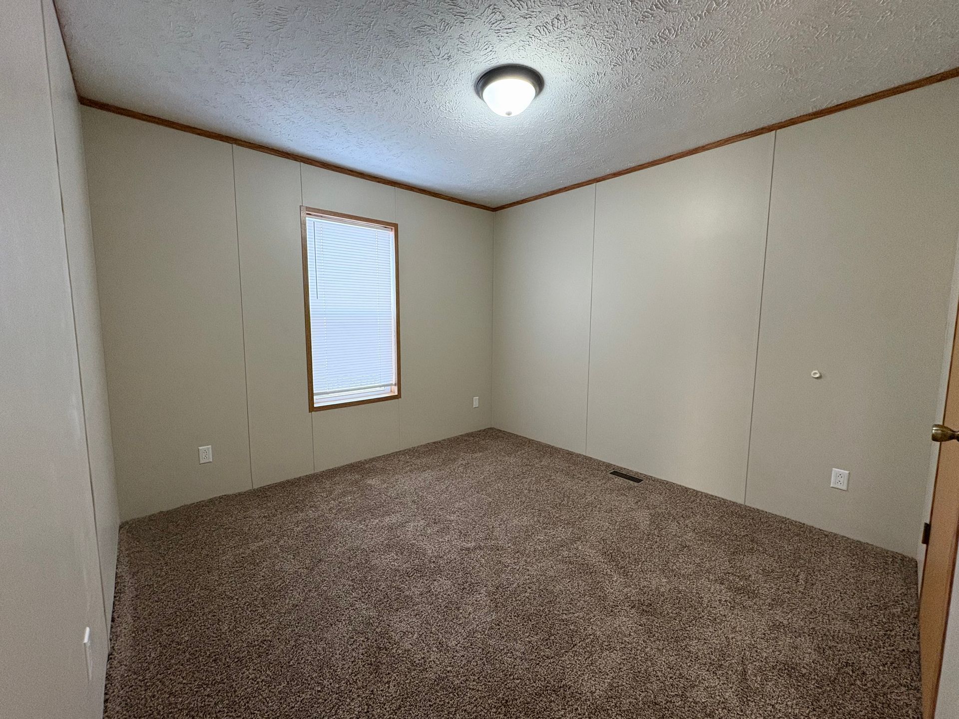 Empty bedroom with beige walls, brown carpet, and a window with blinds.