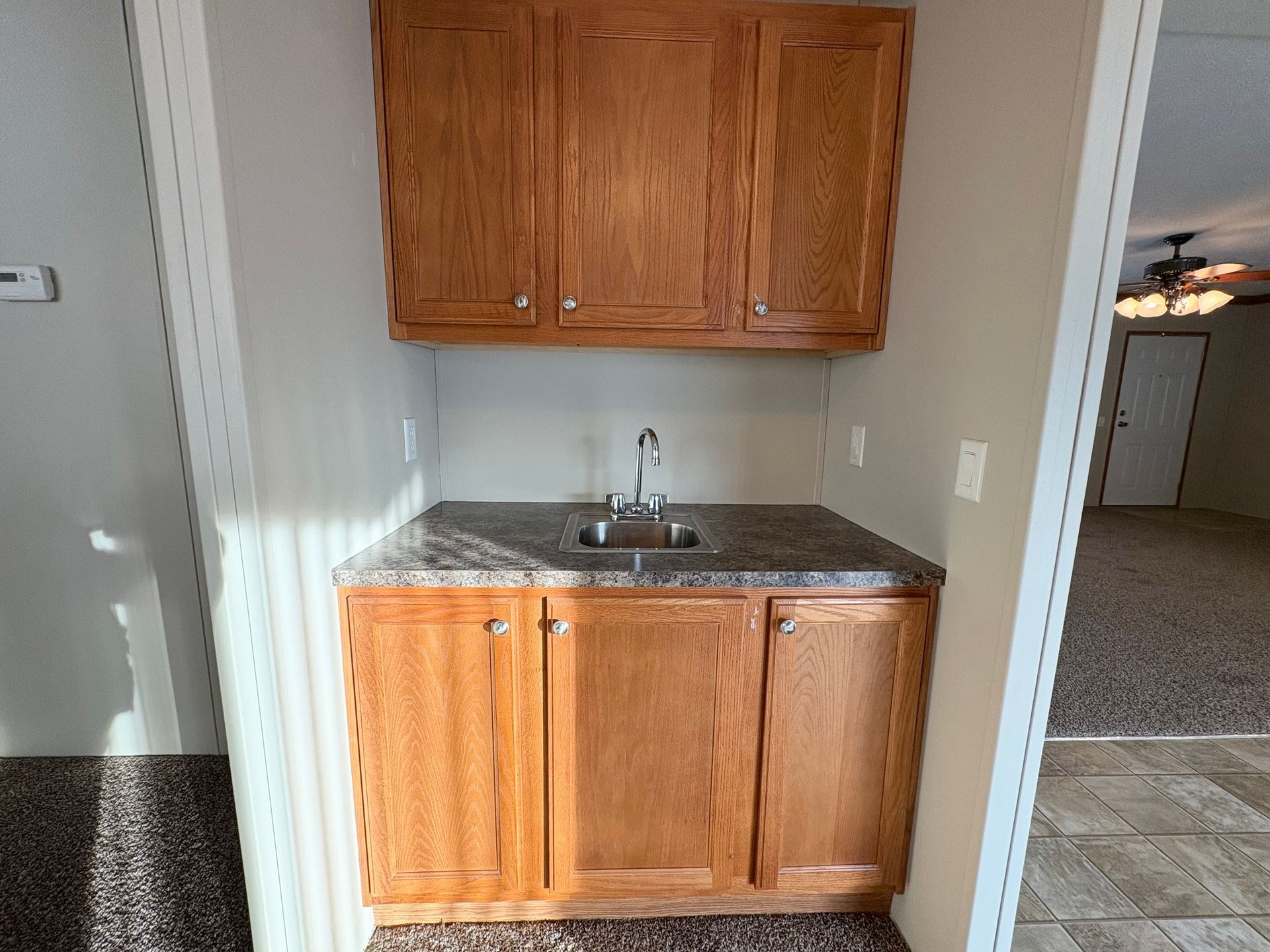 Built-in wood cabinet with sink, countertop, and upper cabinets in a small alcove. Brown and beige.