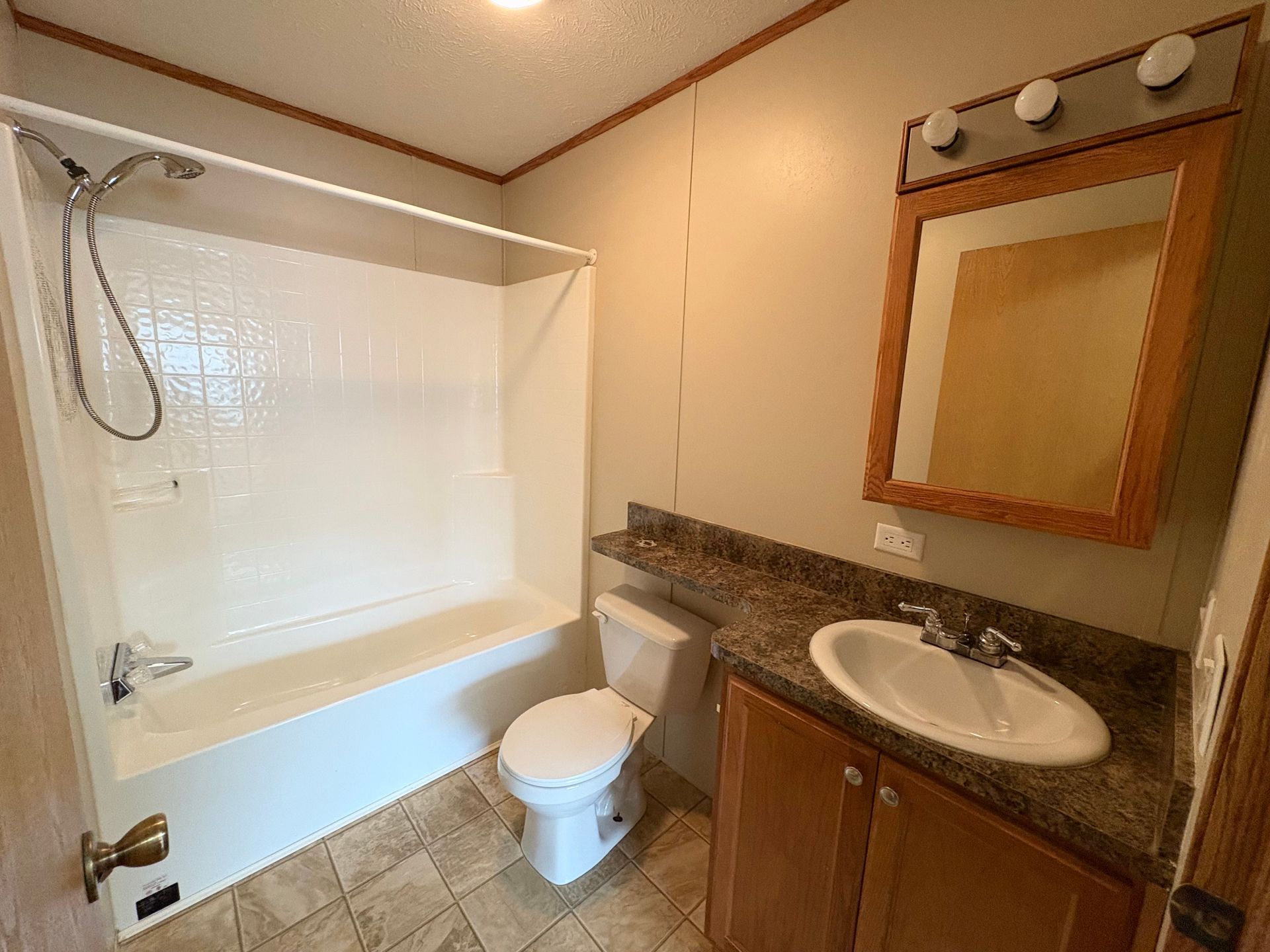 Bathroom with white shower/tub, toilet, vanity with sink, and mirror. Tan walls and floor.