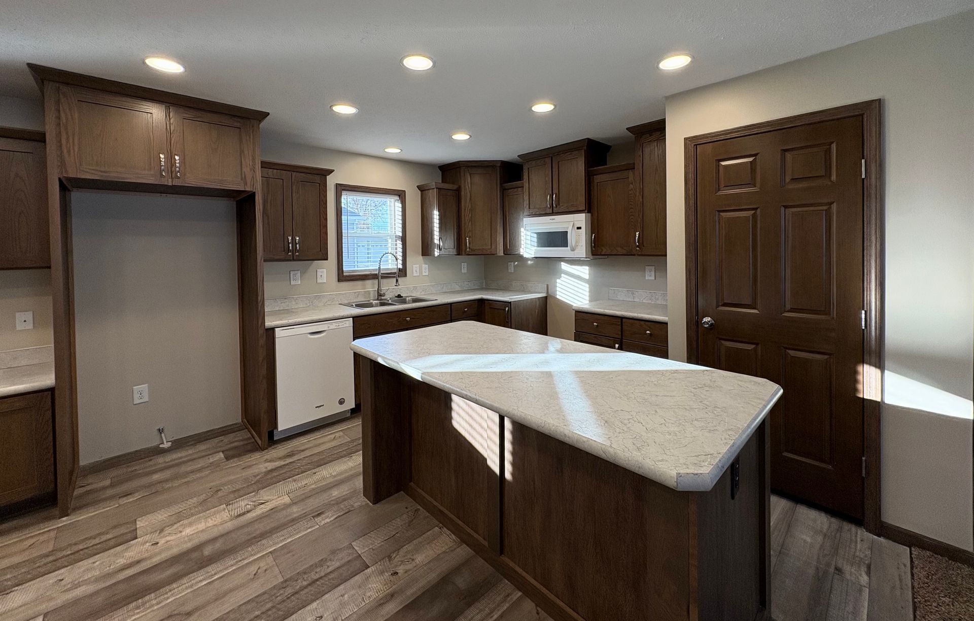 A newly remodeled kitchen with dark brown cabinets, white appliances, and a central island with light-colored countertops.