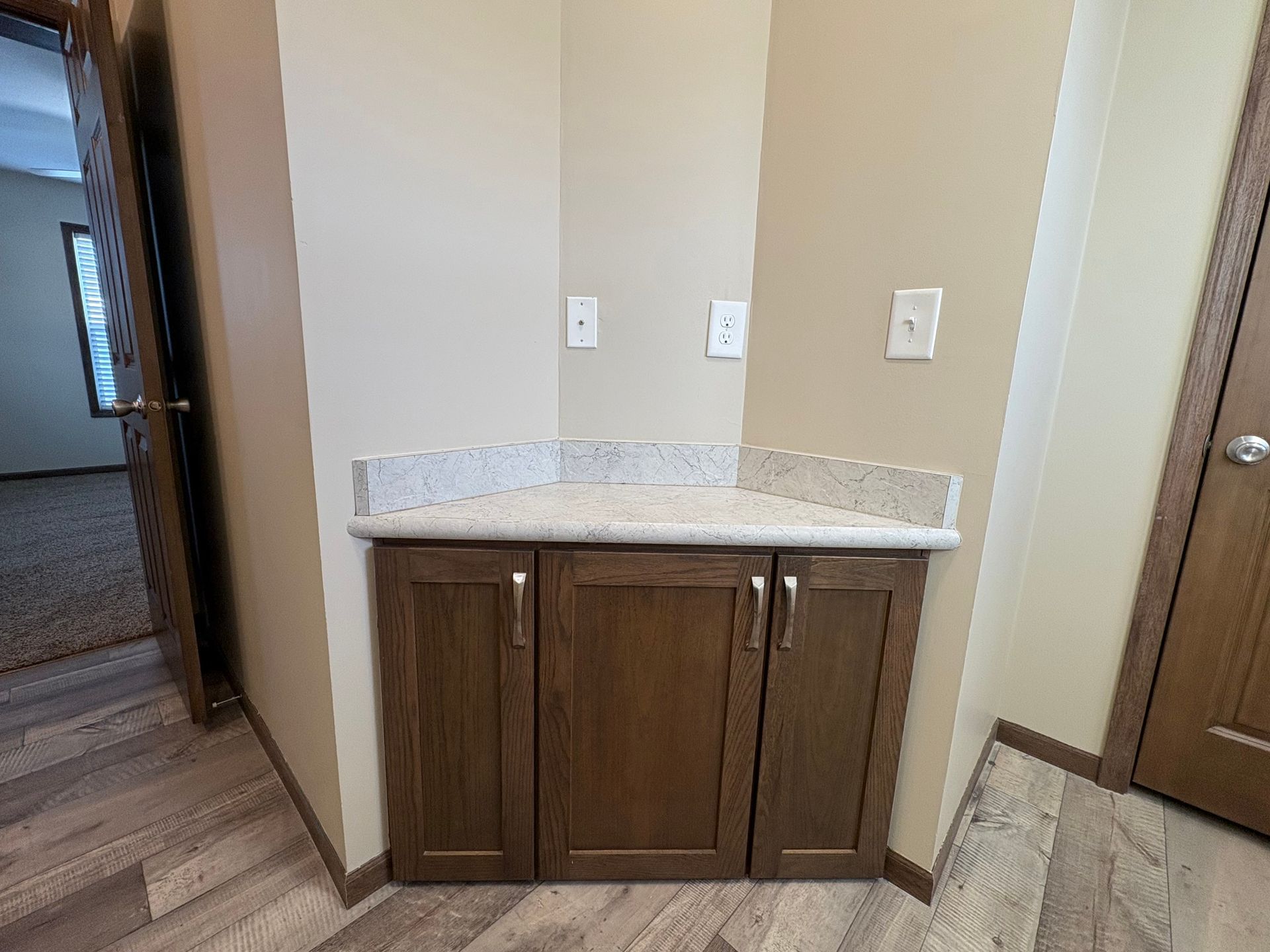 Brown cabinet with light countertop in a corner, with two outlets above and a doorway on the left.