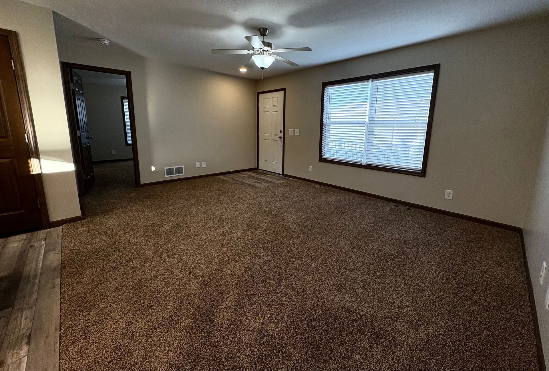 Empty living room with brown carpet, neutral walls, and a large window.