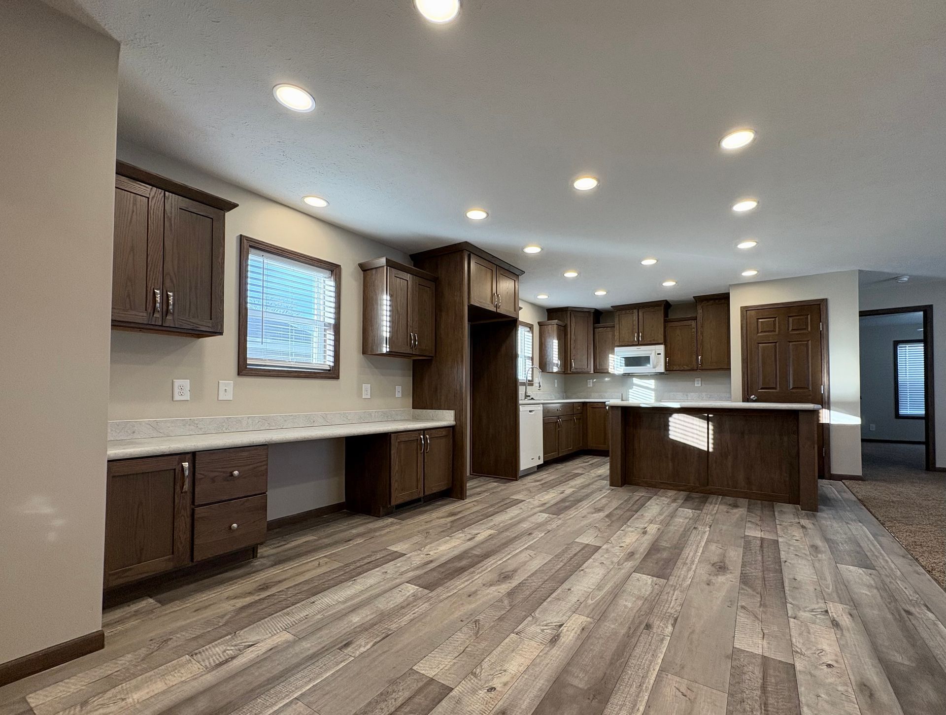 Spacious kitchen with brown cabinets, white countertops, and wood-look flooring. Recessed lighting.