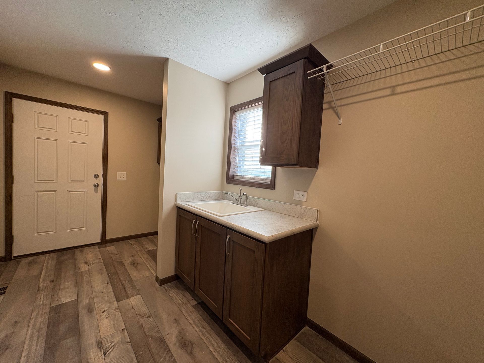 Laundry room with dark cabinets, a sink, and a white door. Wooden floor.