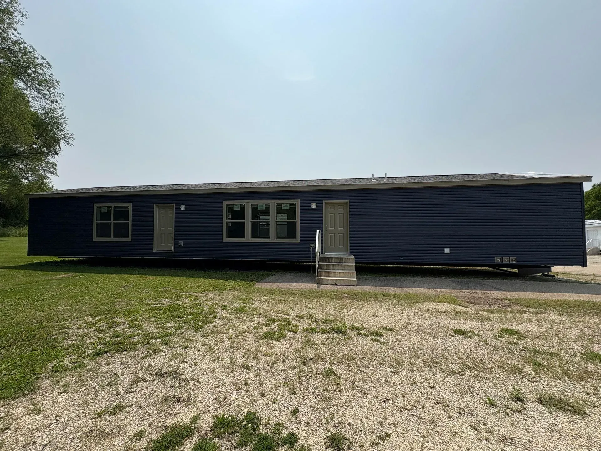 A navy blue mobile home on a grassy lot, with steps leading to a door.