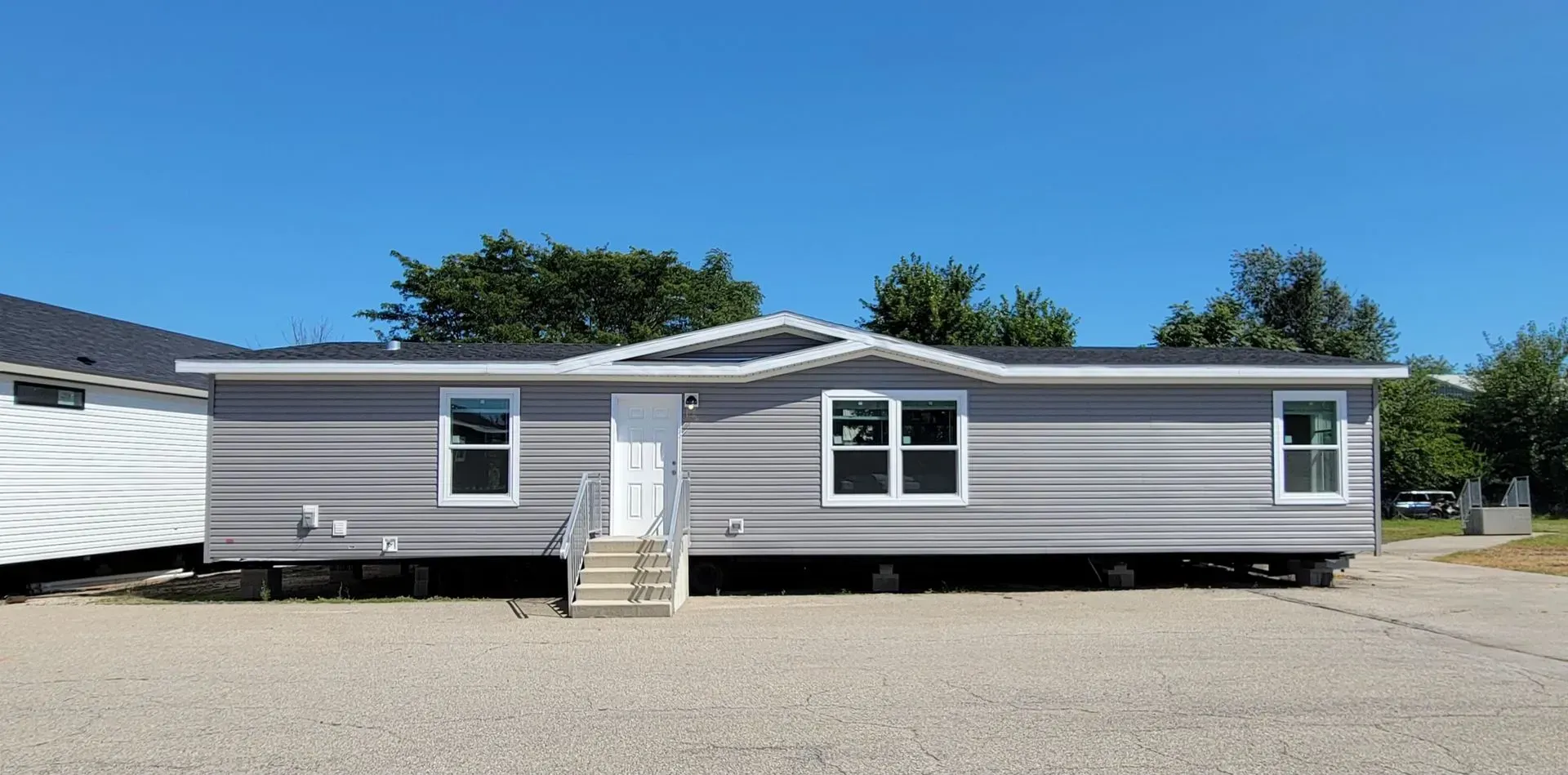 A light grey modular home with white trim and a small staircase. Clear blue sky in the background.