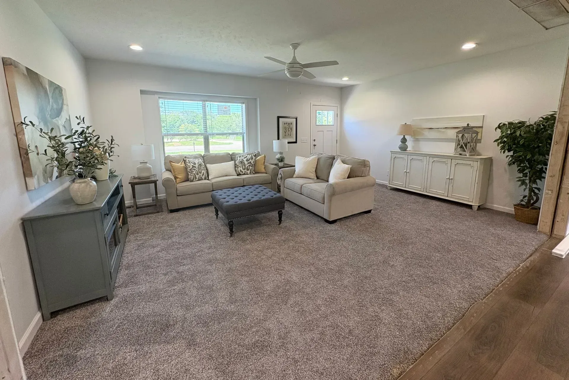 Spacious living room with light-colored carpet, two sofas, a bench, and a large window.