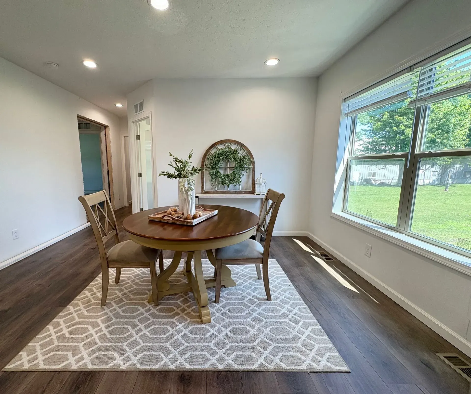 Dining room with round wooden table, two chairs, rug, and window.