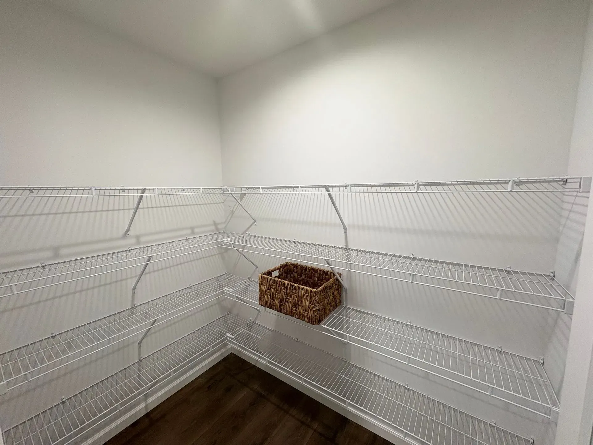 Empty walk-in pantry with wire shelving, brown floors, and a woven basket.