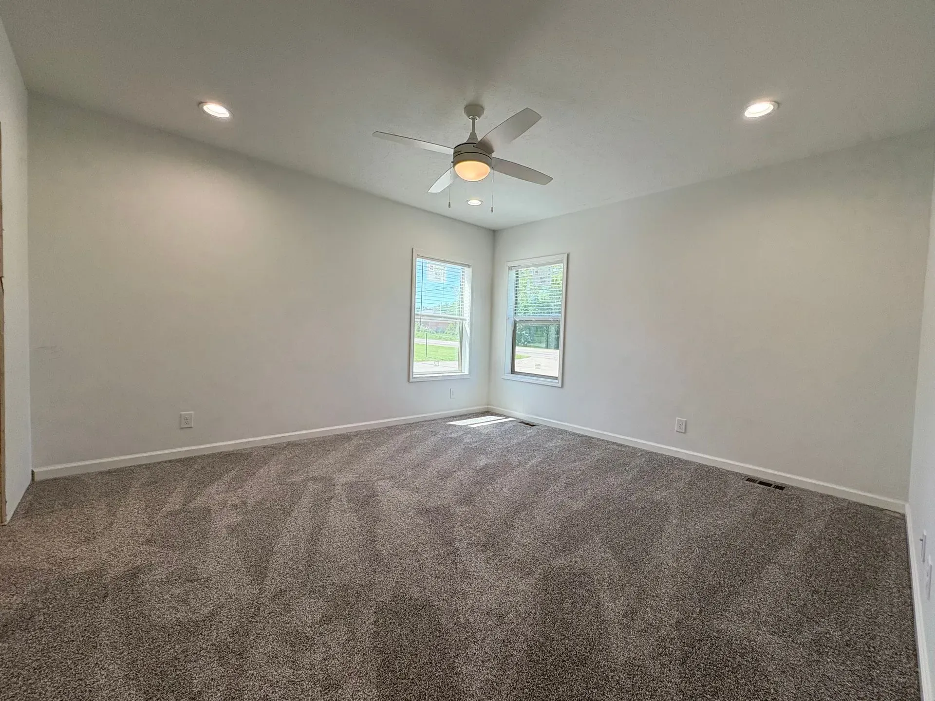 Empty room with gray carpet, white walls, two windows, and a ceiling fan.