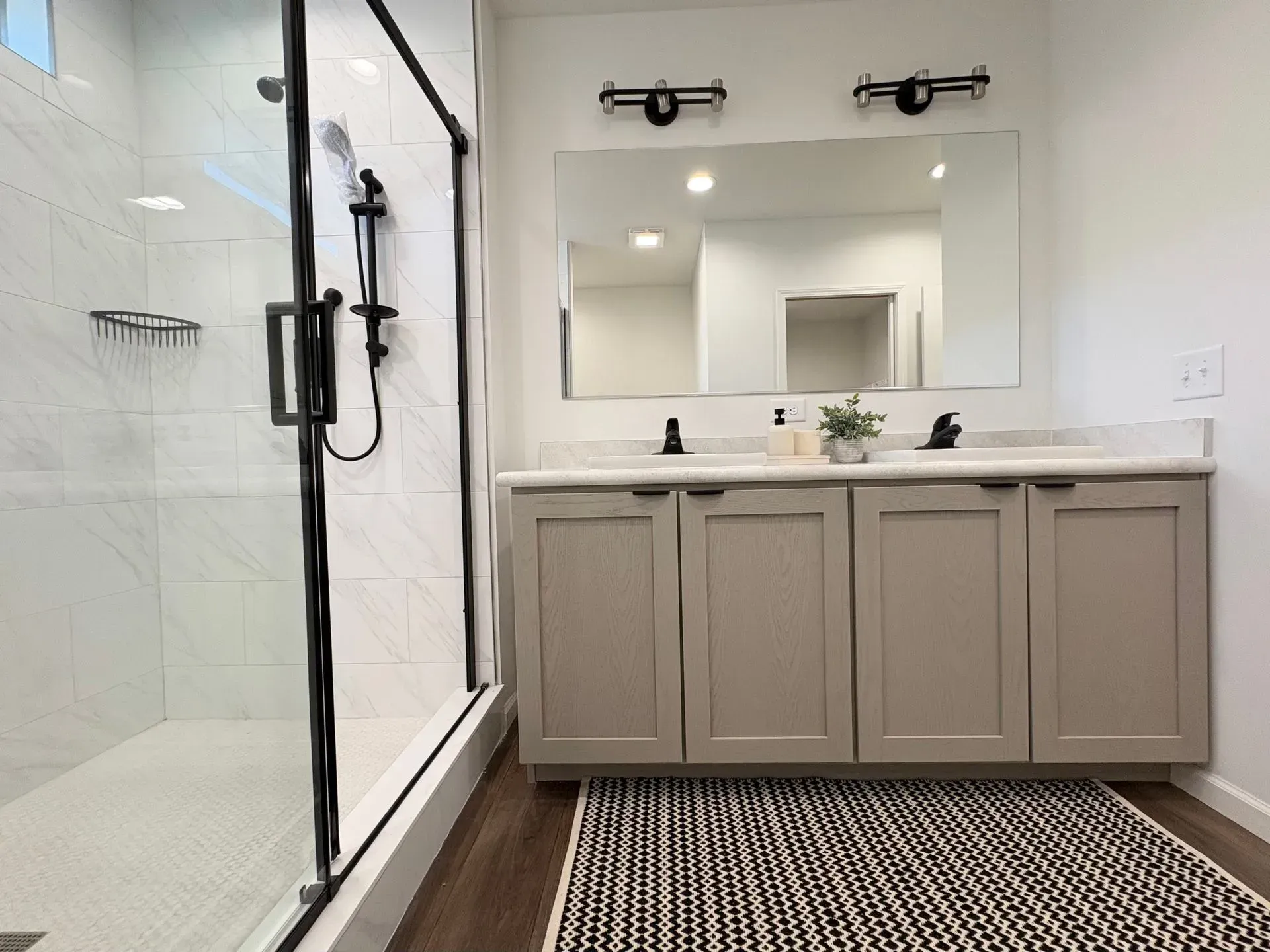 Modern bathroom with glass shower, double vanity, and a black and white rug.