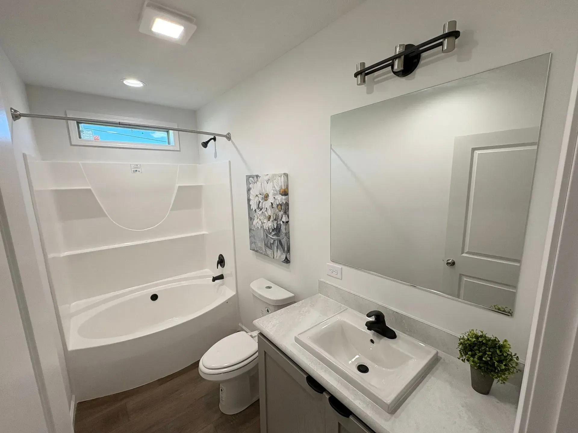 Bathroom with white fixtures, grey vanity, large mirror, and wood-look flooring.
