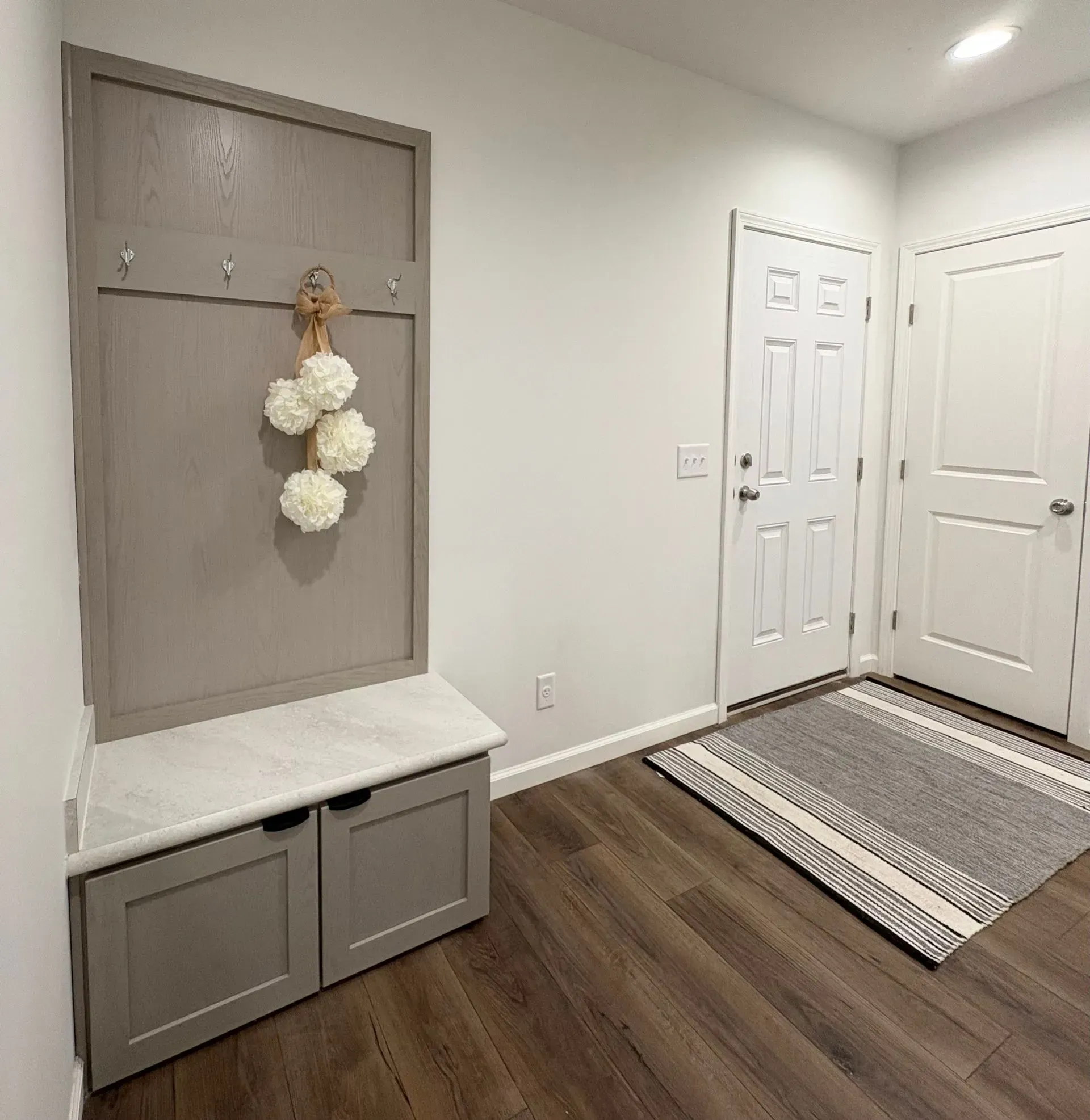 Gray entryway with a bench, coat rack, white doors, and a rug.