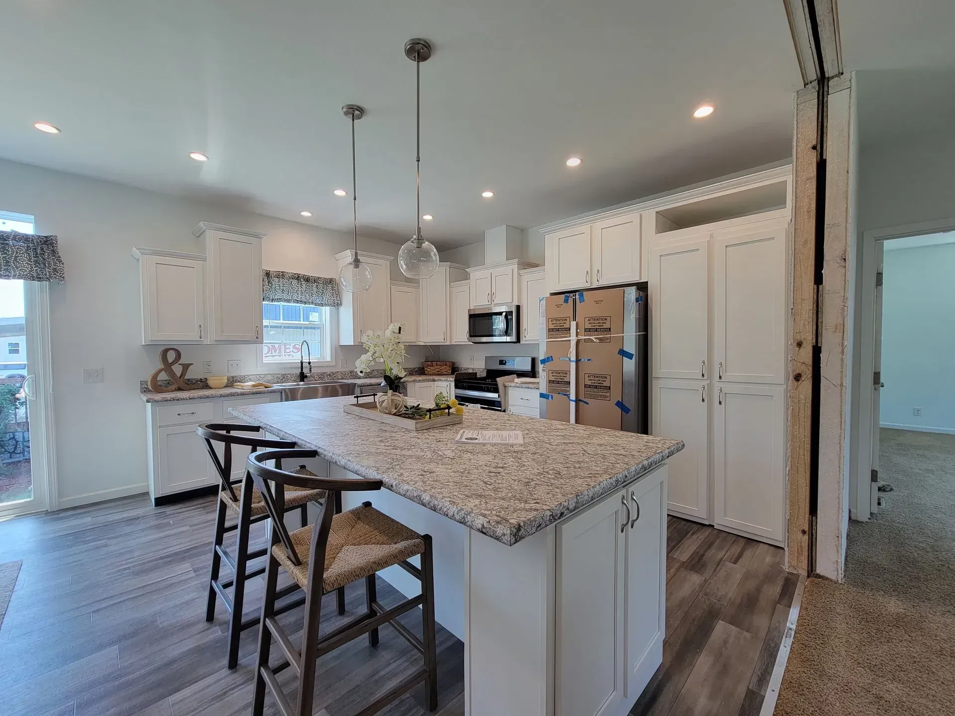 Spacious white kitchen with an island, cabinets, and appliances. Bar stools and decorative lights are present.