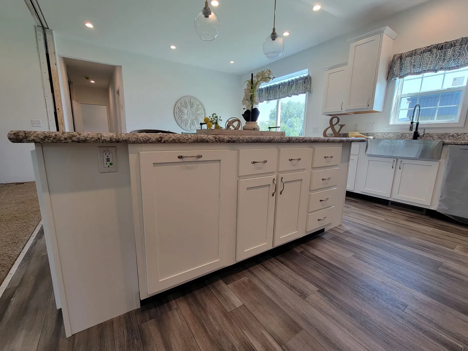 White kitchen island with a granite countertop and cabinets, near a window and sink.