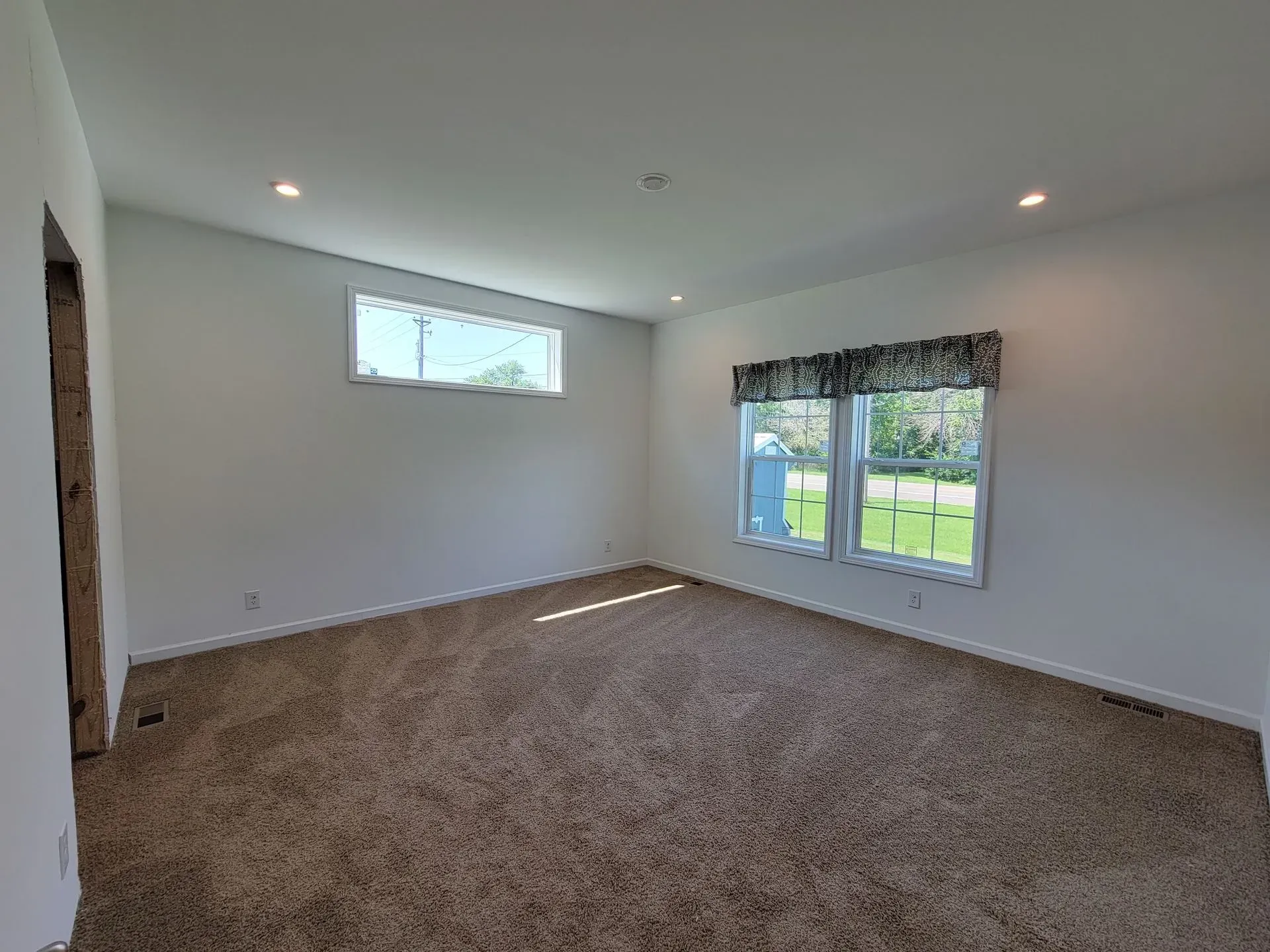Empty room with brown carpet, two windows, and recessed lighting.