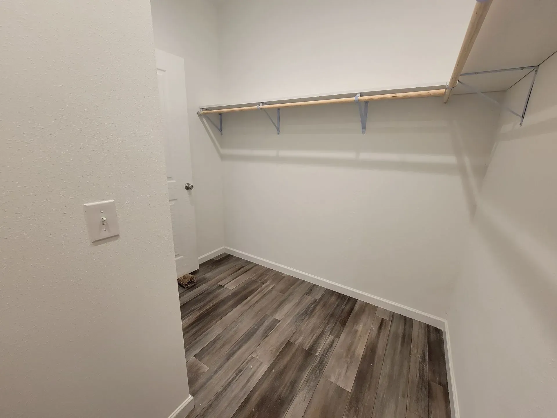 Empty closet with wood-look floor, white walls, a shelf, and a door in the background.
