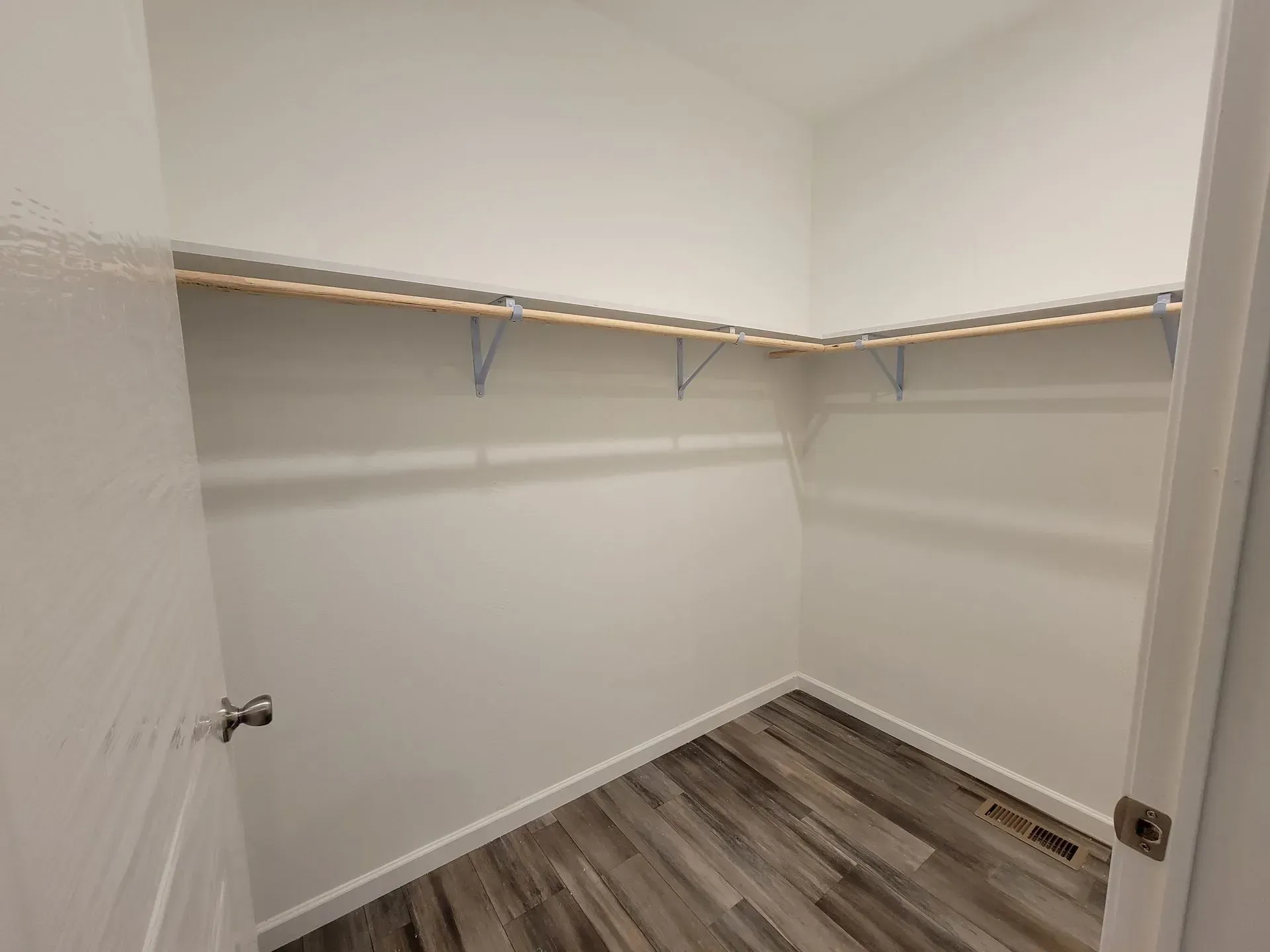 Empty white walk-in closet with wood shelves and flooring; door is partially open.