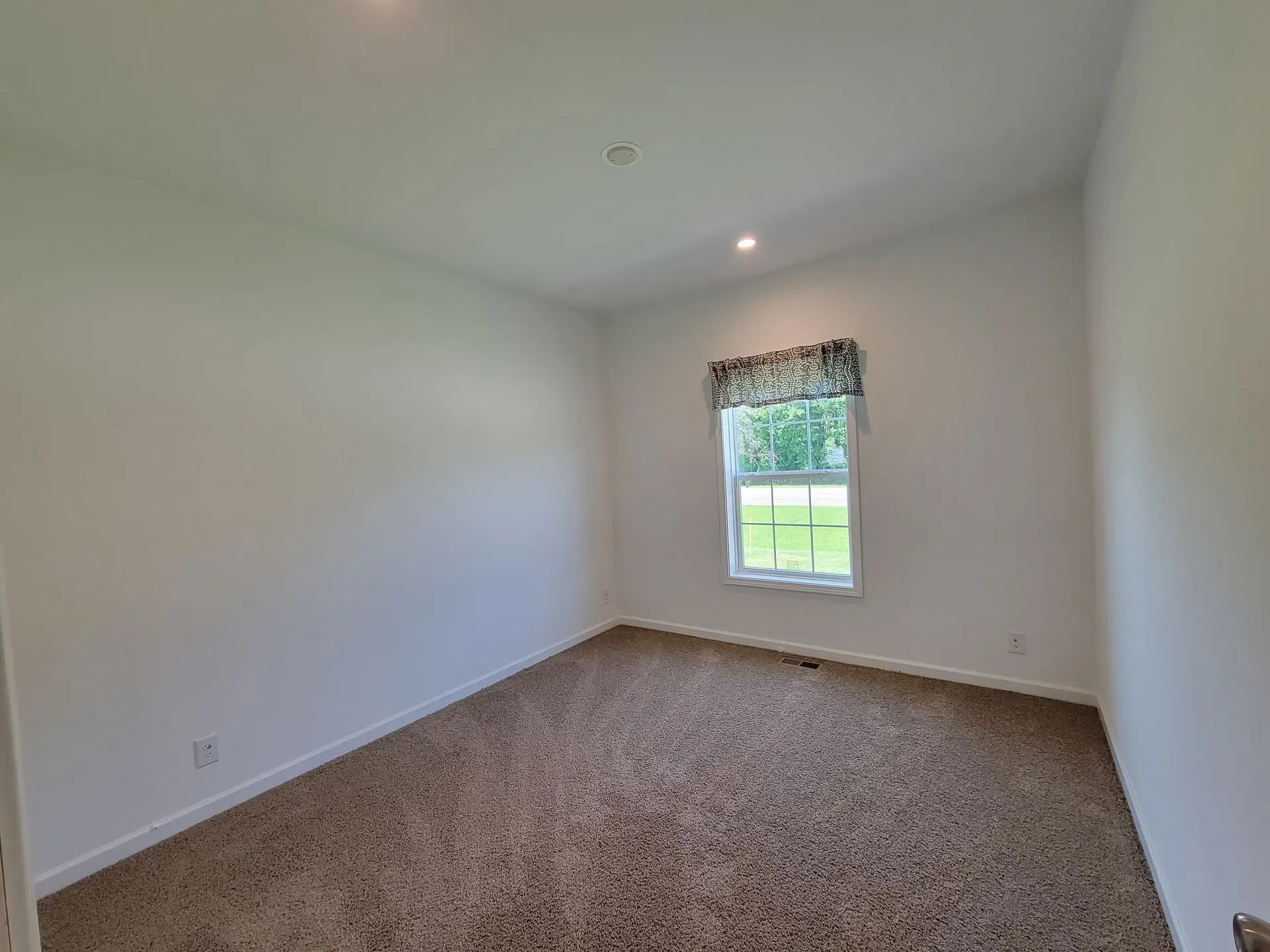 Empty room with brown carpet, white walls, and a window with a valance.