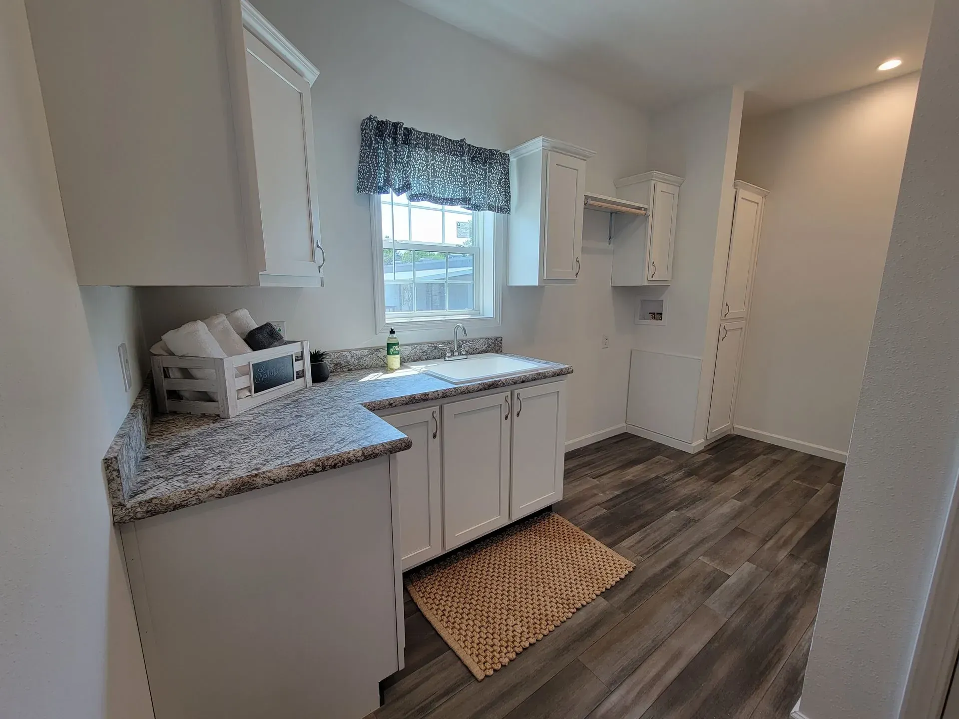 Kitchen with white cabinets, granite countertops, and wood-look flooring. Window with floral valance.