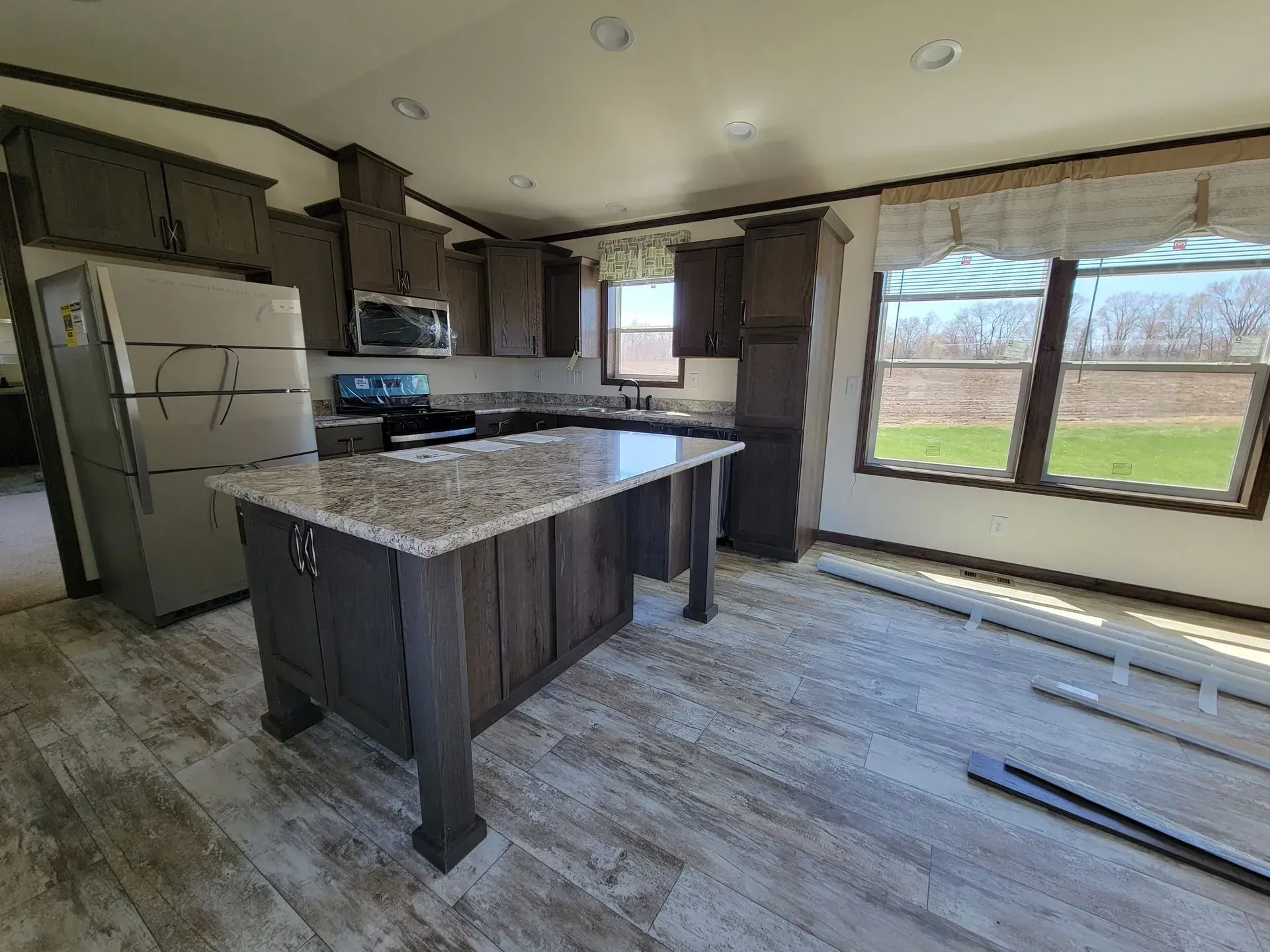 Kitchen with dark wood cabinets, island, and stainless steel refrigerator. Windows with light curtains.