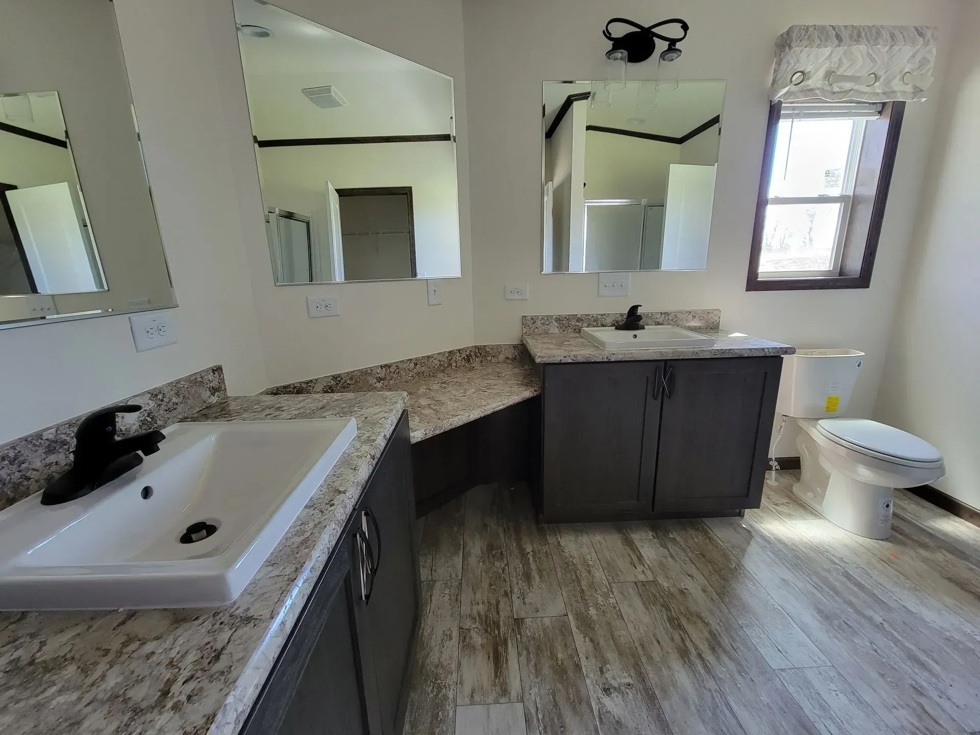 Bathroom with two sinks, a toilet, and mirrors. Gray cabinets, light countertops, and wood-look flooring.