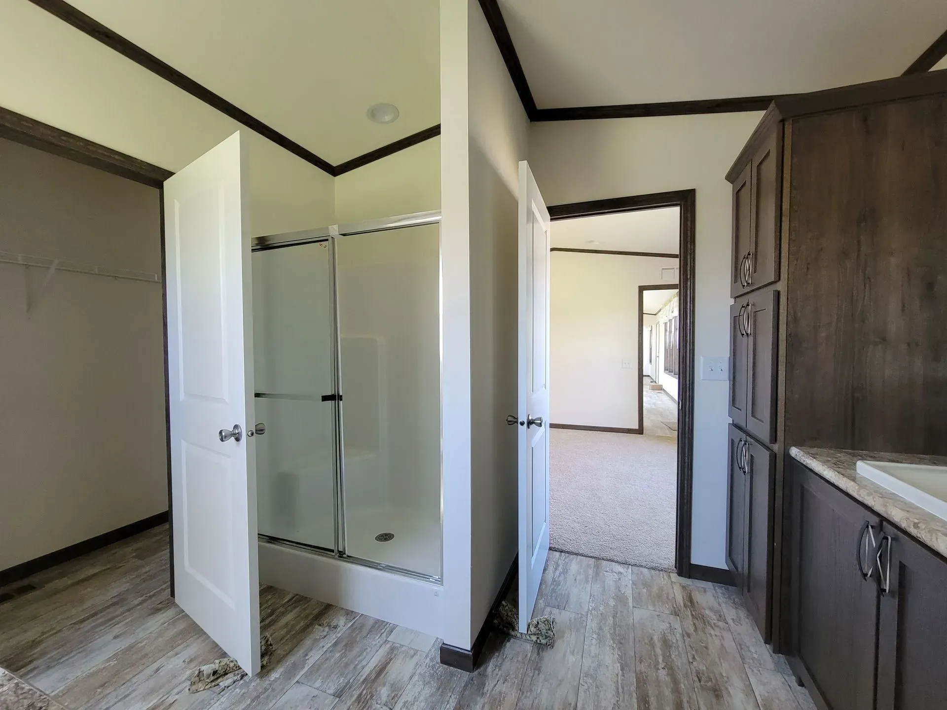 Bathroom with shower, door, and cabinets; neutral colors and wood-look flooring.