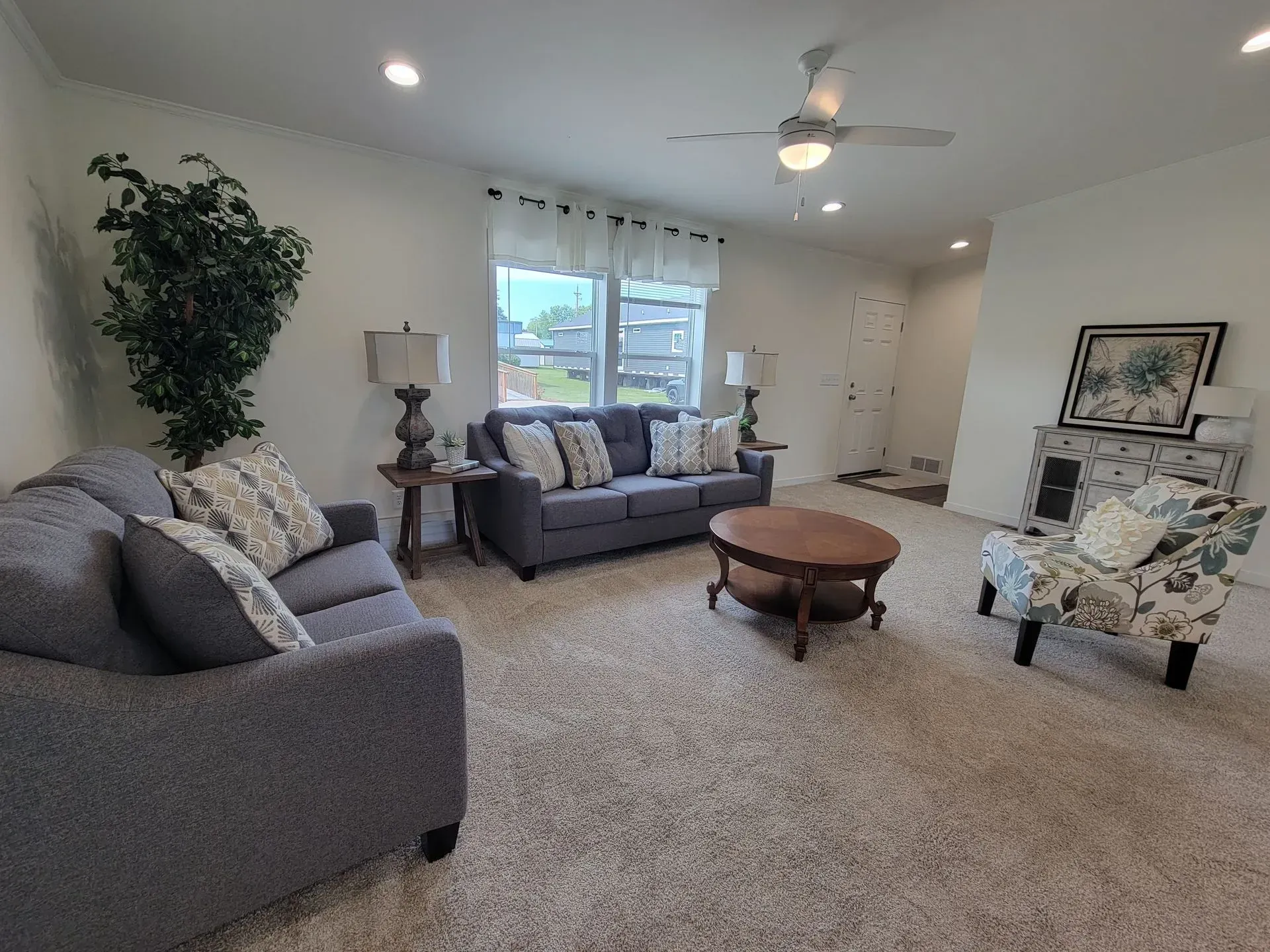 Living room with gray sofas, floral chair, coffee table, and large window.